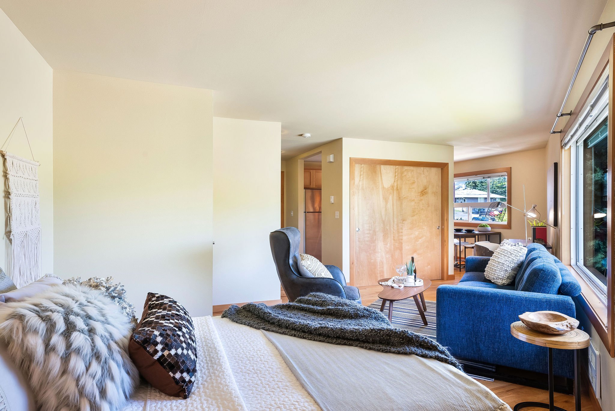  Image description: interior of studio with couch, armchair, queen bed, desk and large window 