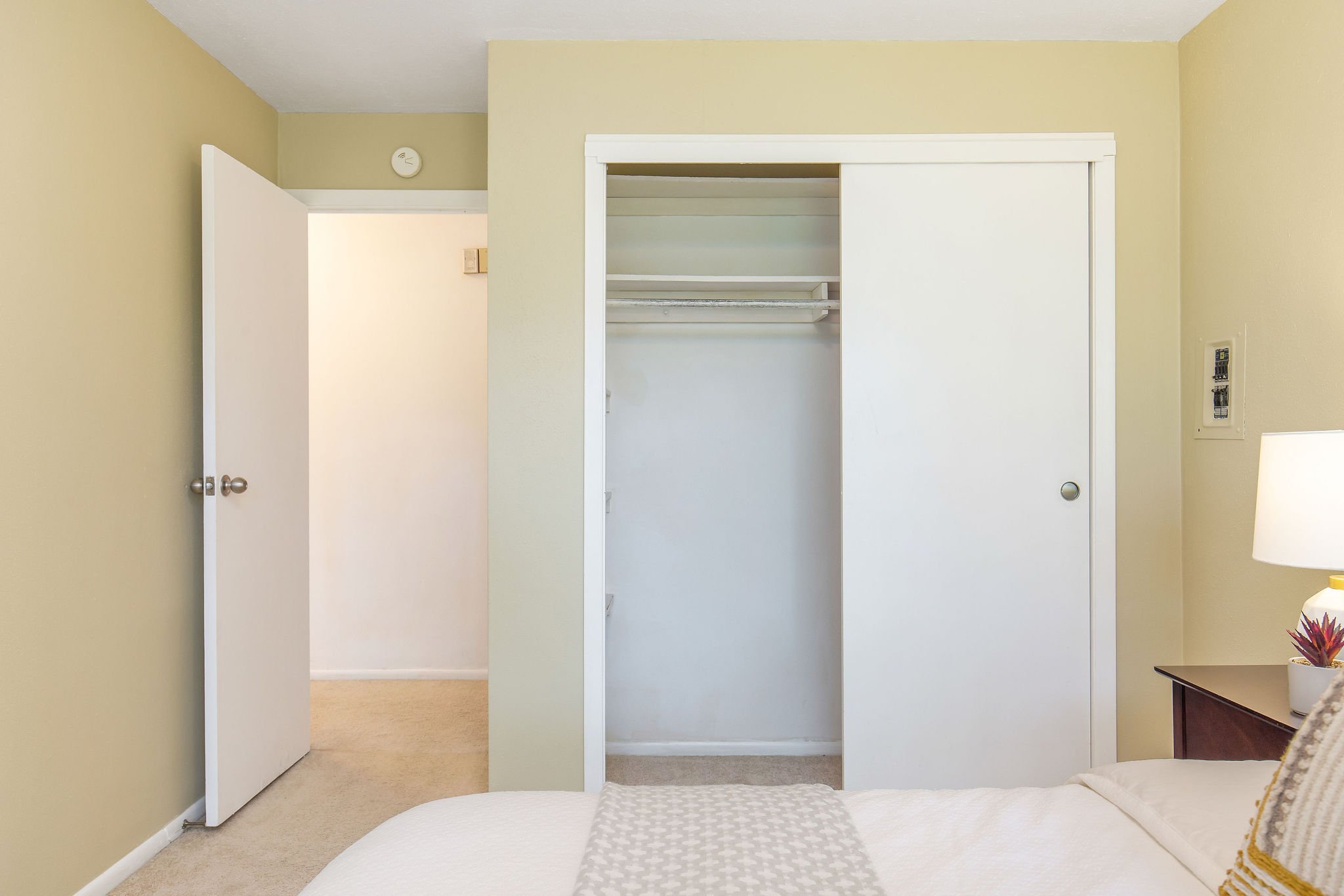  image description: interior of bedroom with queen bed, closet, and tan carpet 