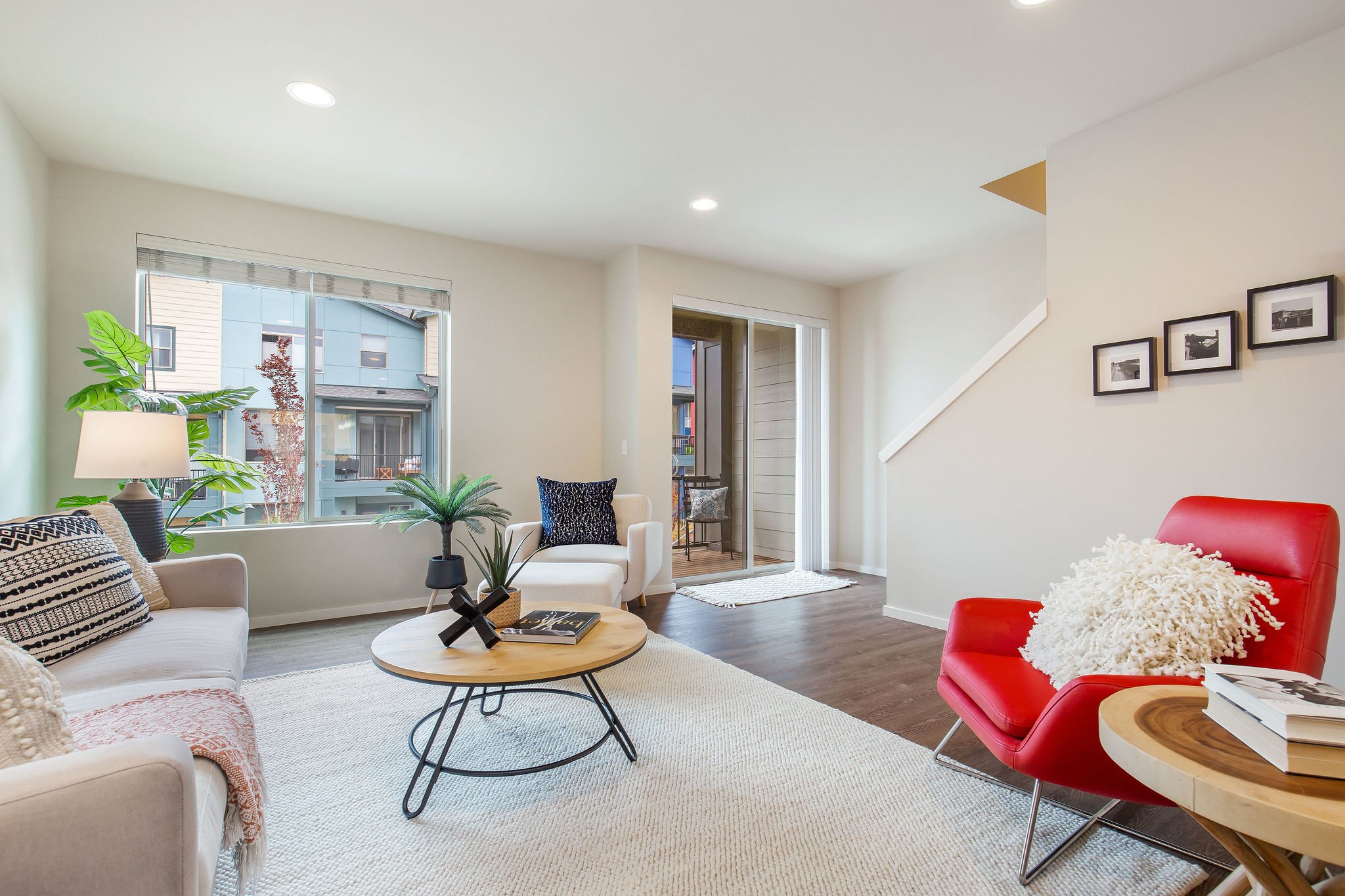  image description: interior of living room with hardwoods, large window, couch, rug and chairs 