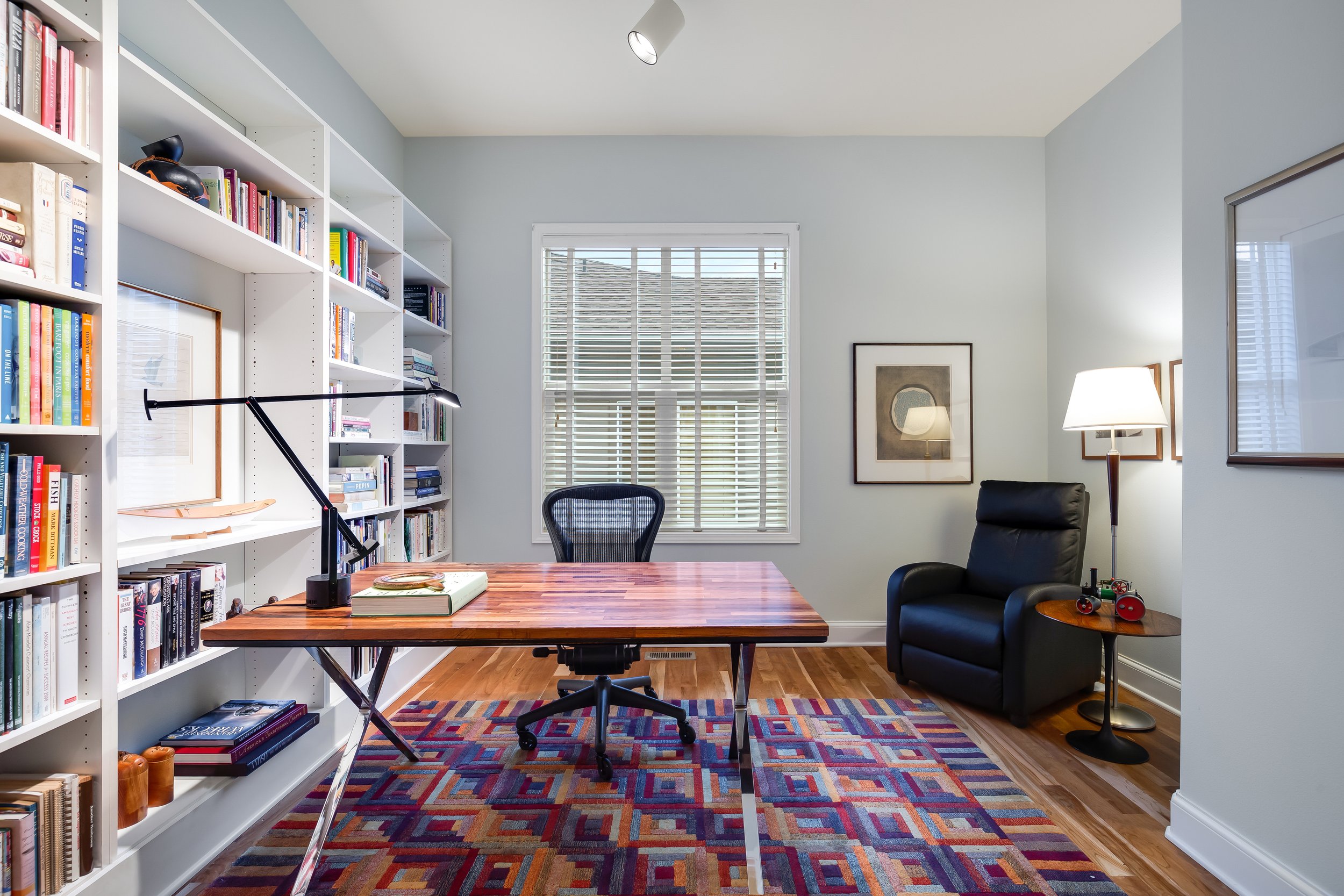  interior of office with large bookshelf, window, rug, and desk with chair 