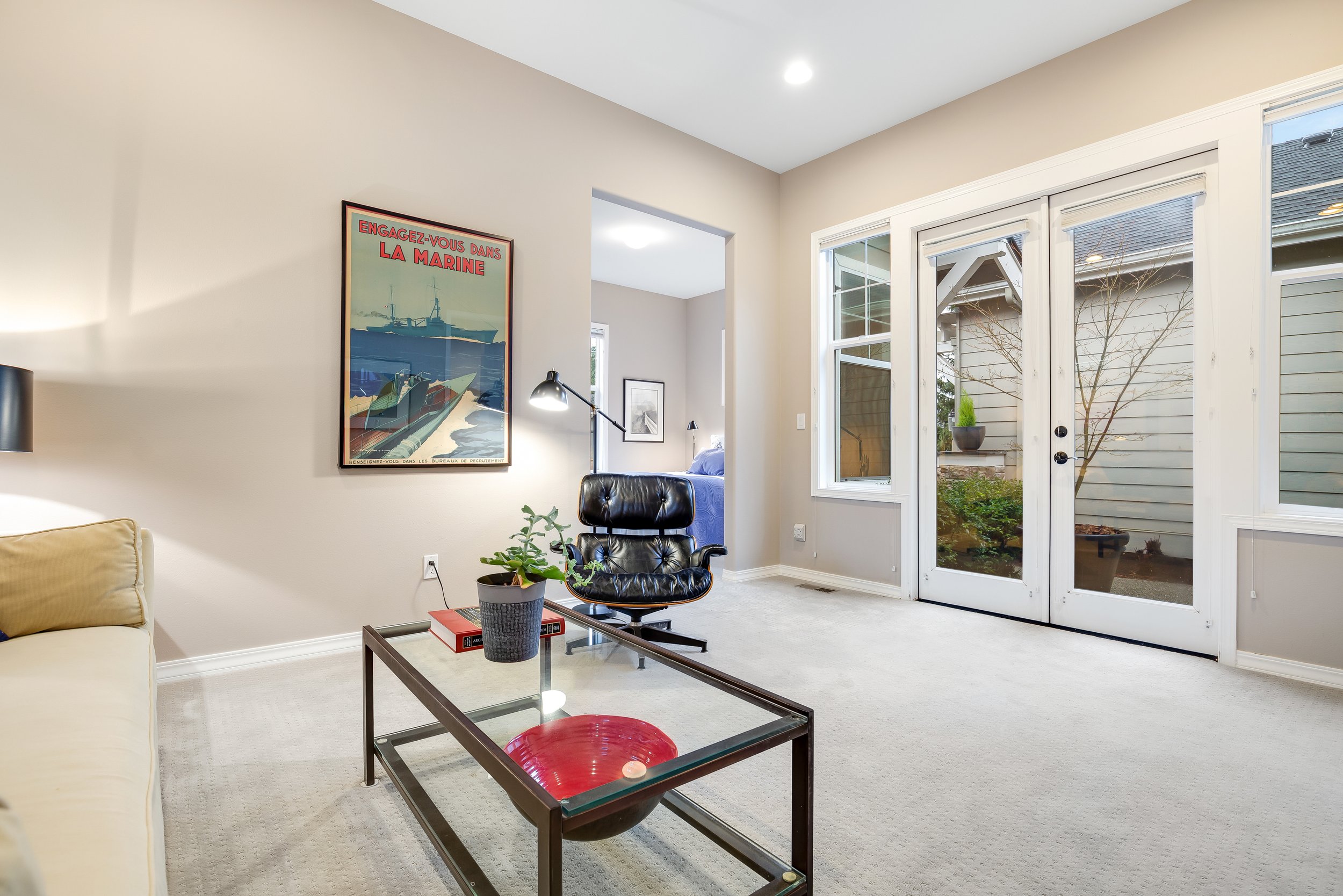  interior of second living room with two small windows, carpet, chairs, and couches and french doors 