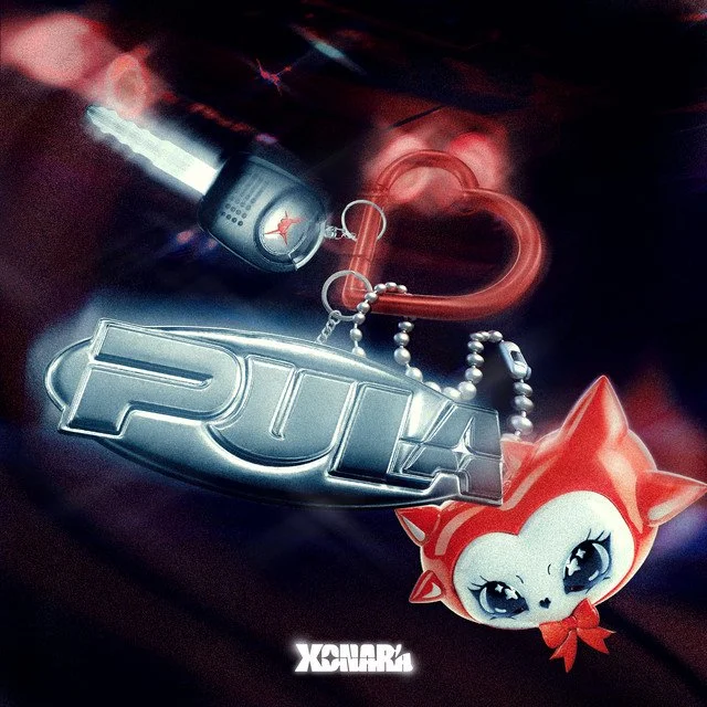 Air freshener hanging from a car's rearview mirror, featuring a red and white cartoon cat with big eyes and a red bow, a silver 'PUNK' tag, and a fan badge with a unicorn logo, against a dark blurred background.