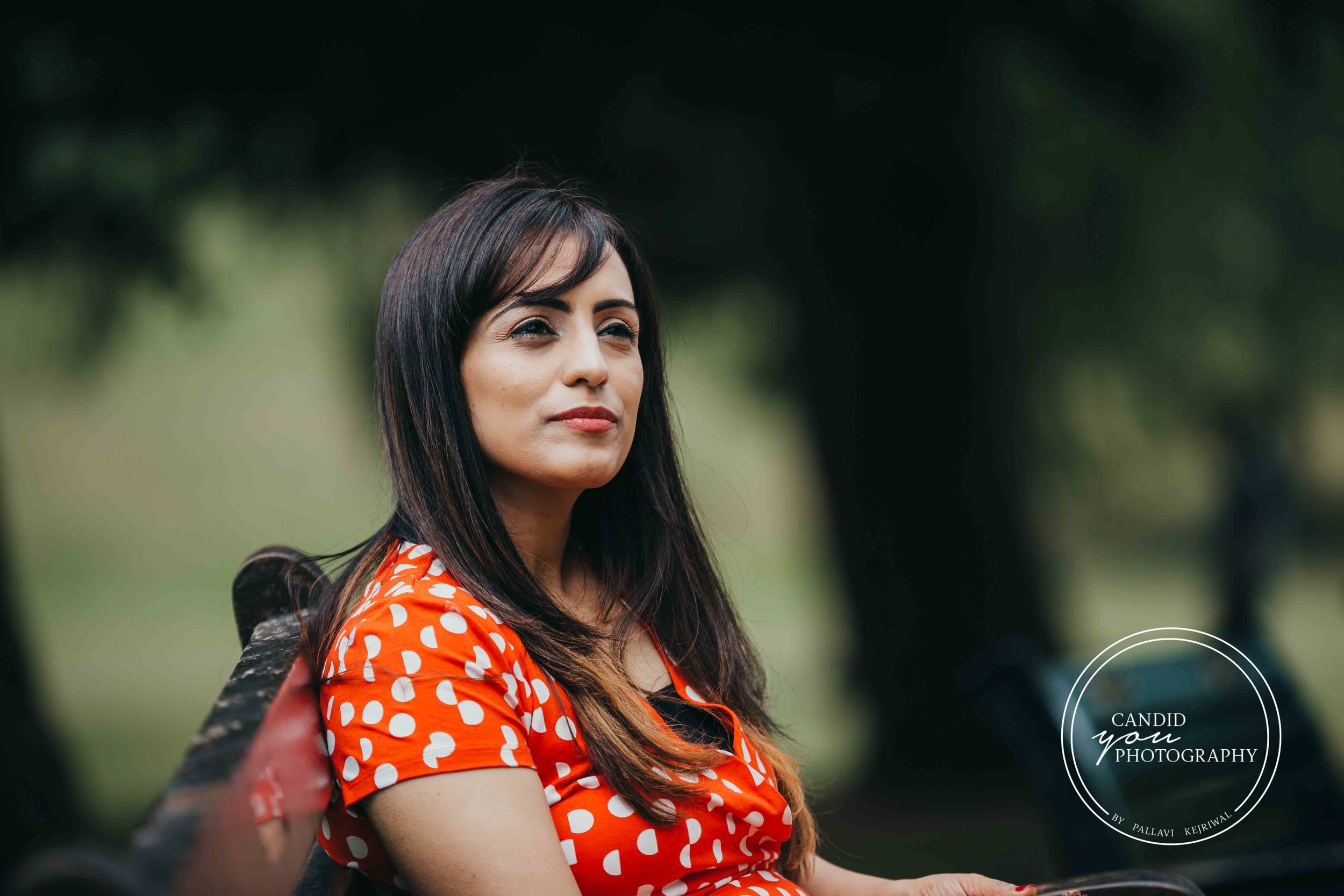 Beautiful lady sitting on park bench in orange polka dot dress