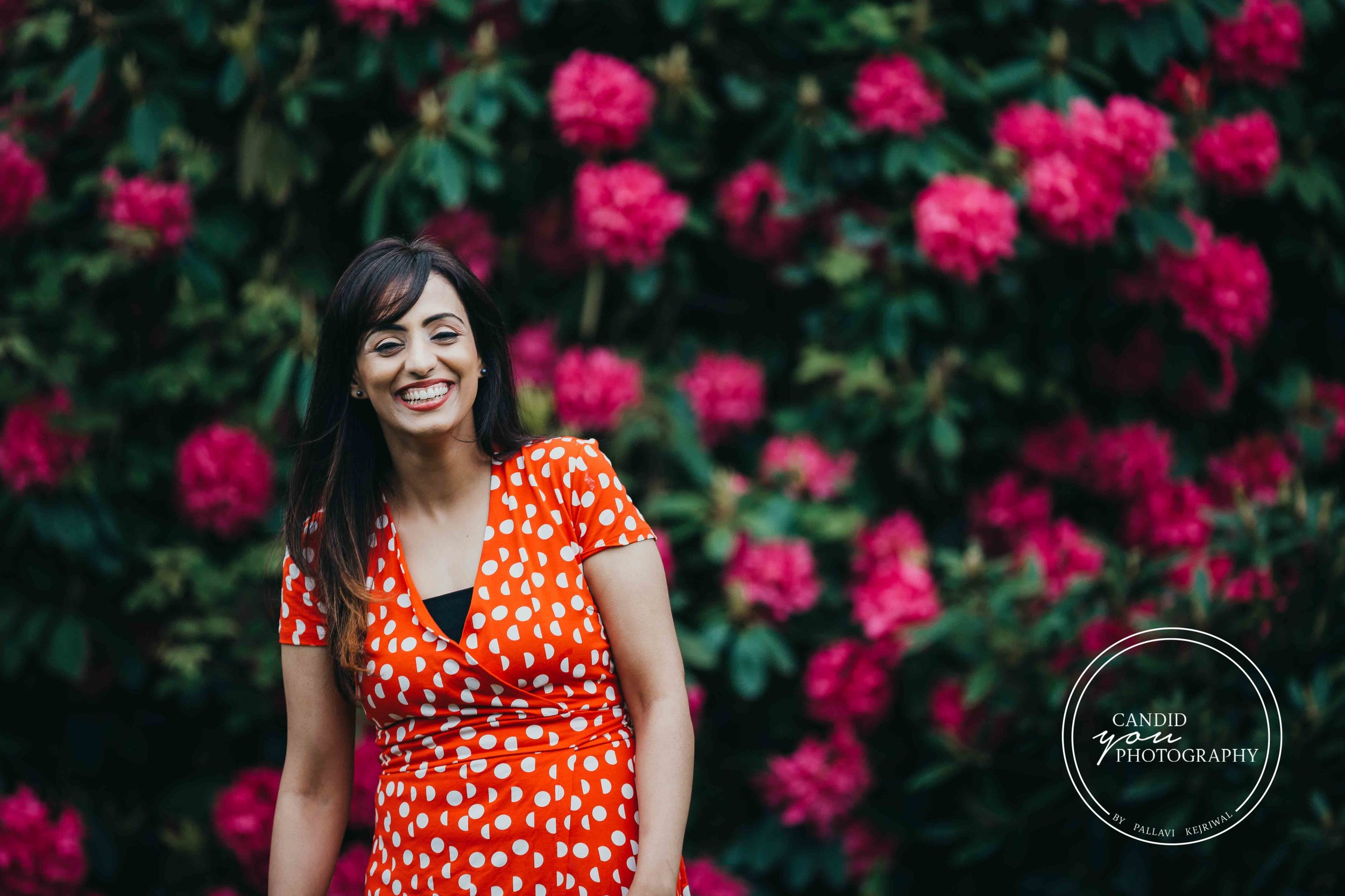 lady laughing in orange polka dot dress in front of pink flowers