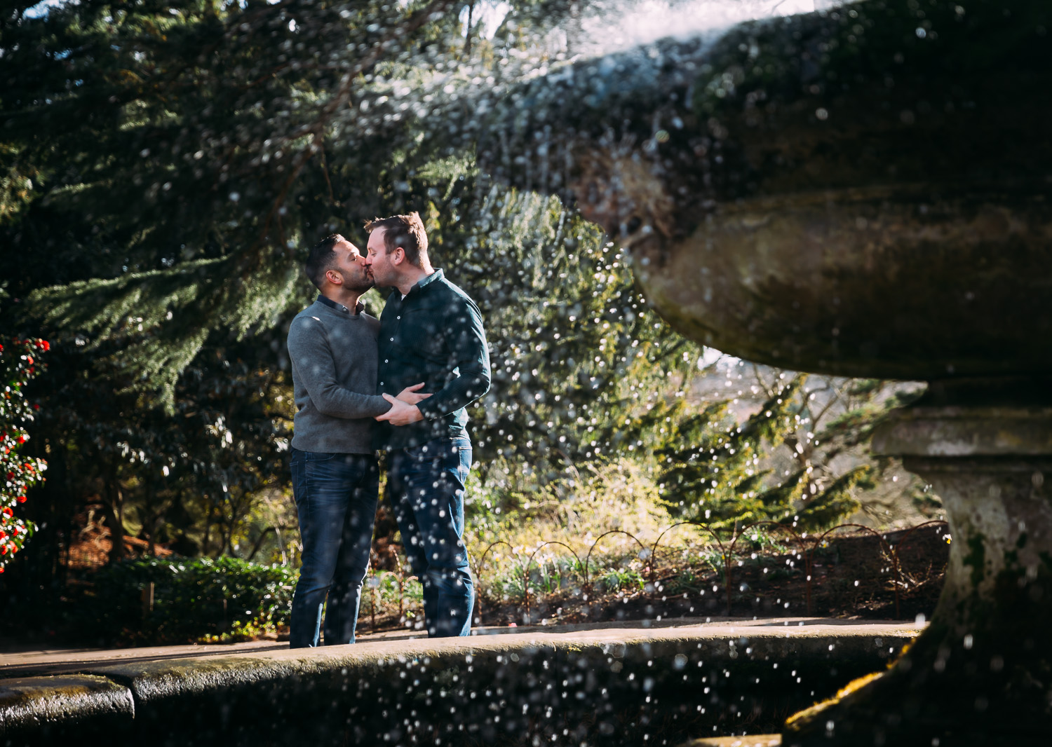 LGBTQ couple kissing near fountain in botanical gardens