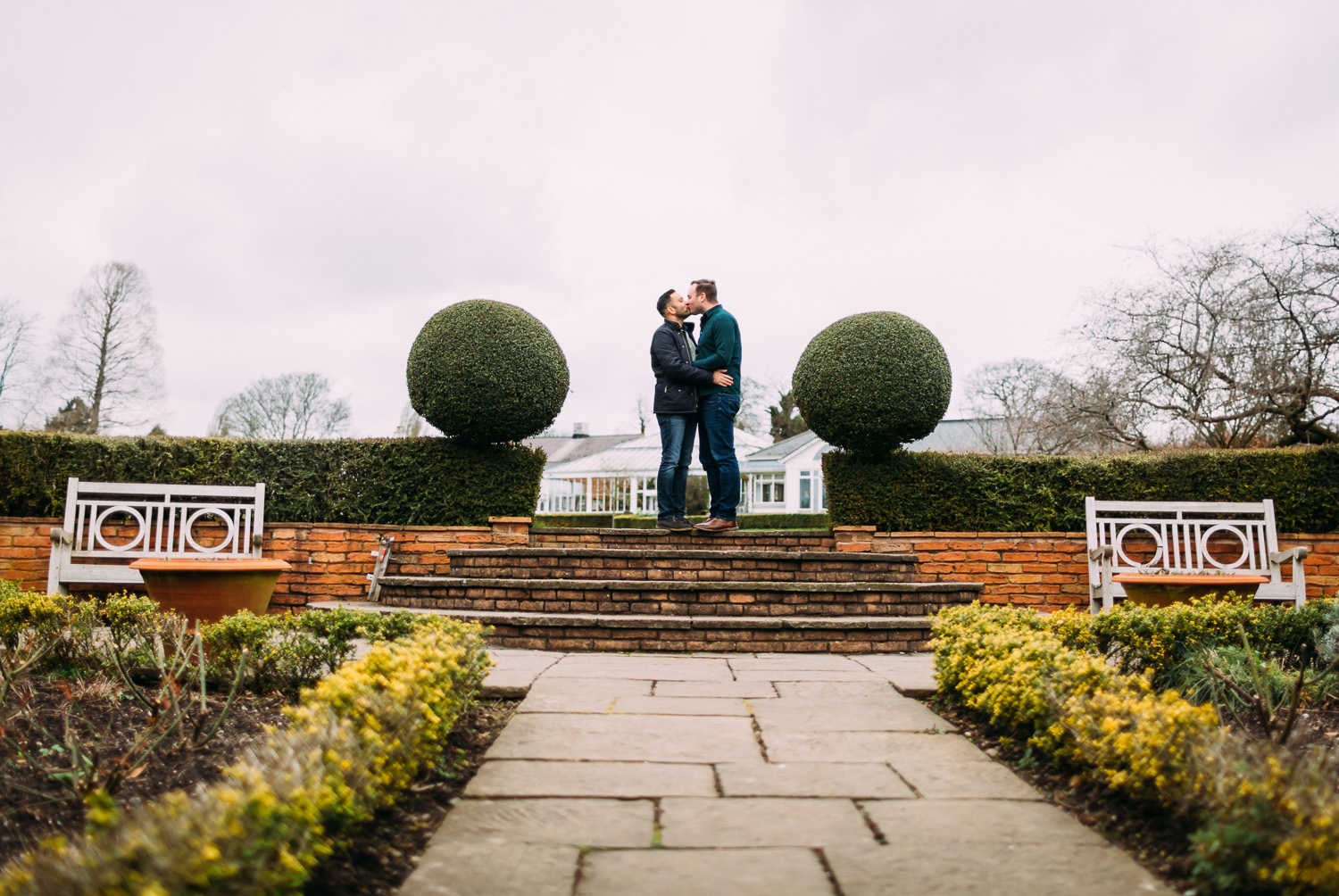 LGBTQ couple kissing near fountain in botanical gardens