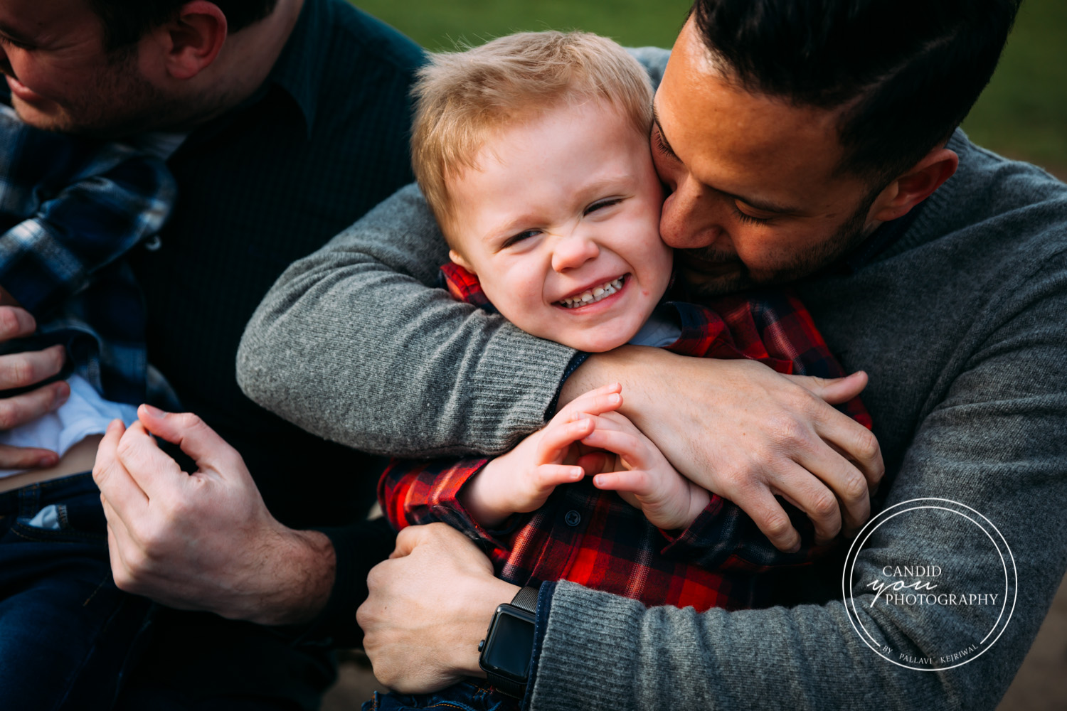 Dad tightly hugs laughing giggling son in park