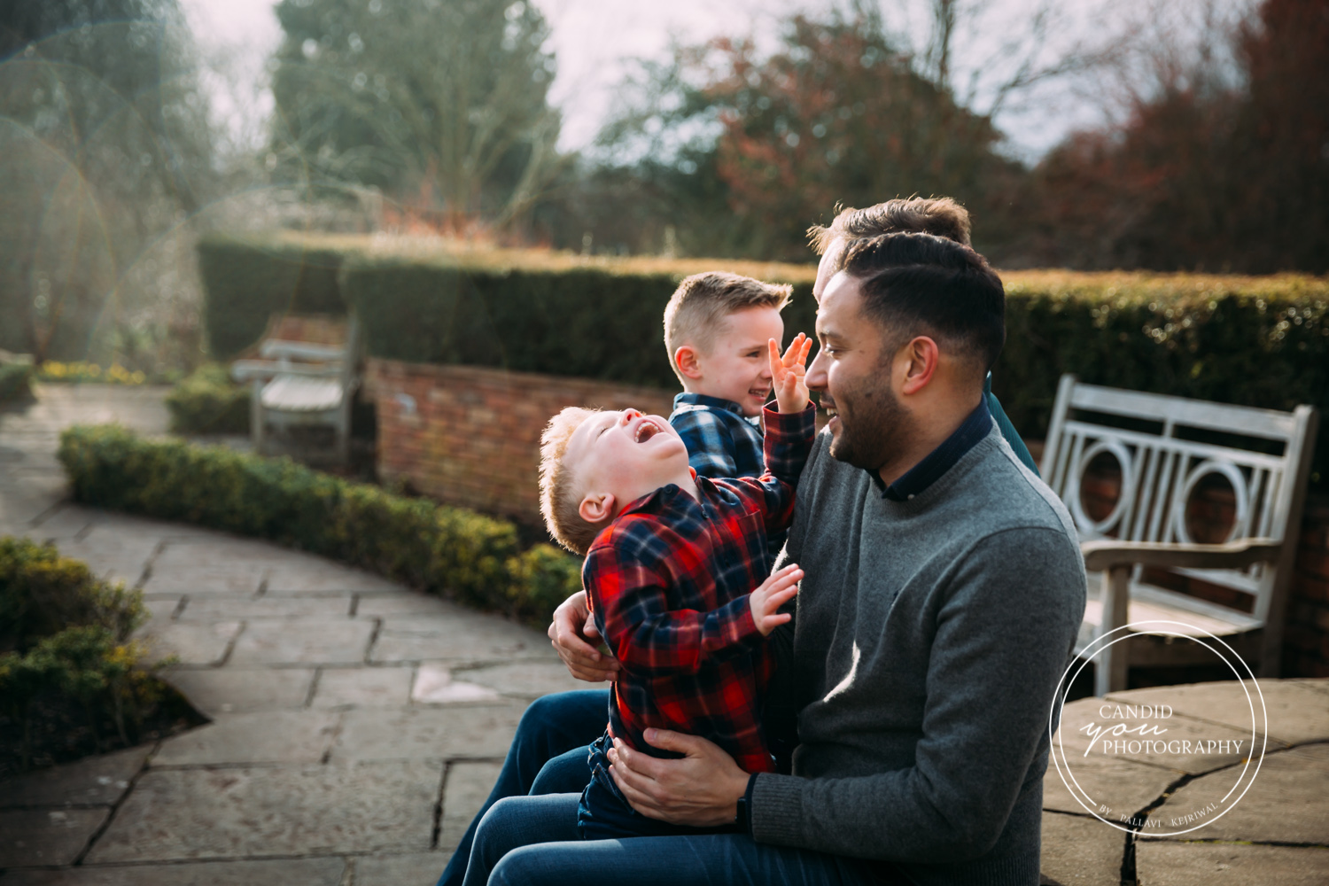 boys giggle uncontrollably while sitting on dad's laps and against setting sun