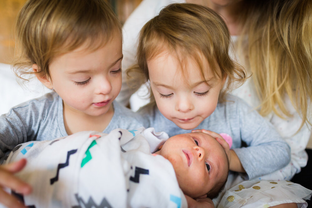 twin girls looking at newborn baby sister
