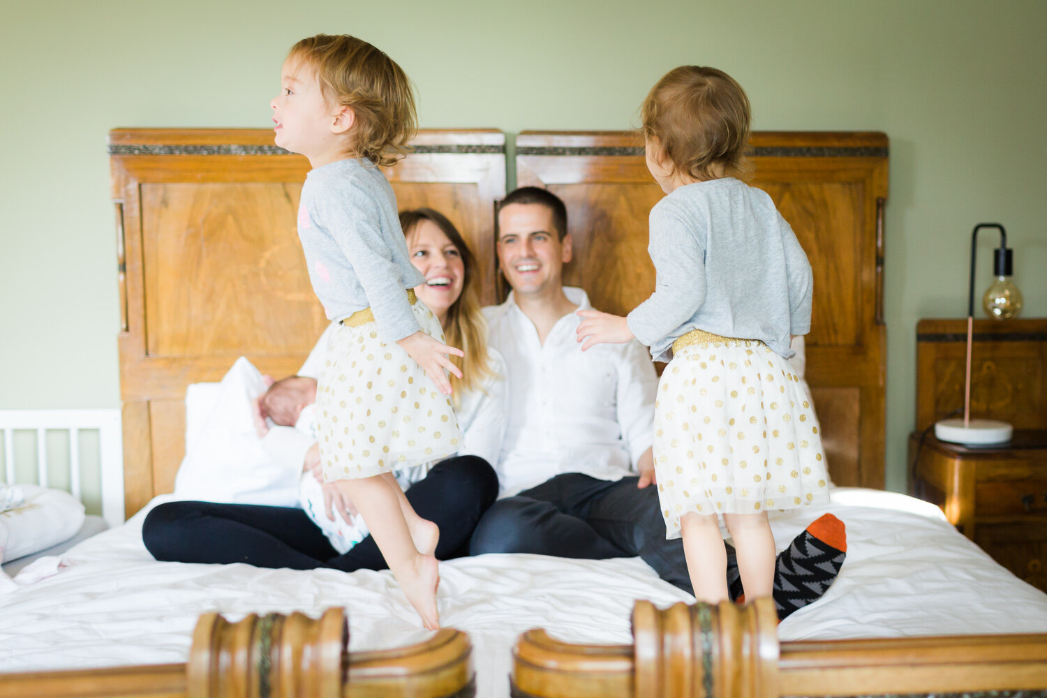 twin girls jumping on bed while parents laugh in birmingham