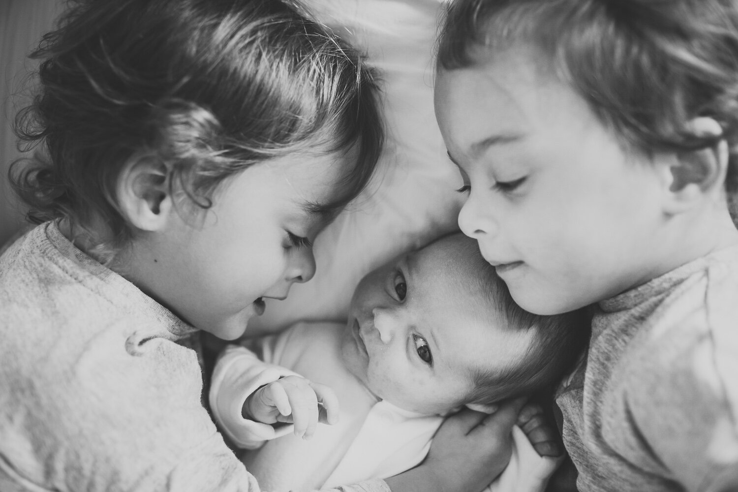 Twin baby sisters cuddling newborn baby sister in edgbaston