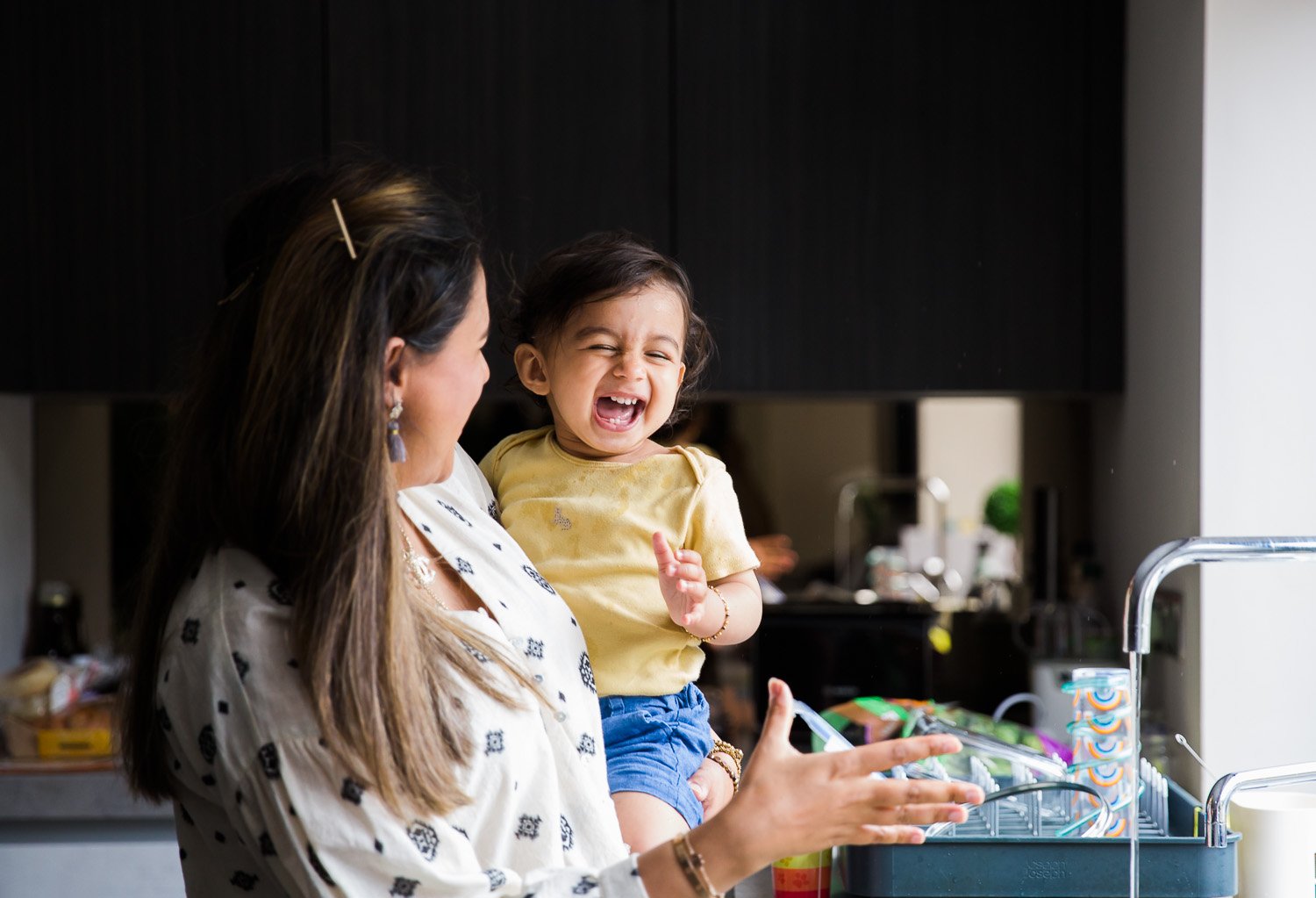 In-Home Family Photo Session In Wimbledon with kid laughing wonderfully while mum looks on