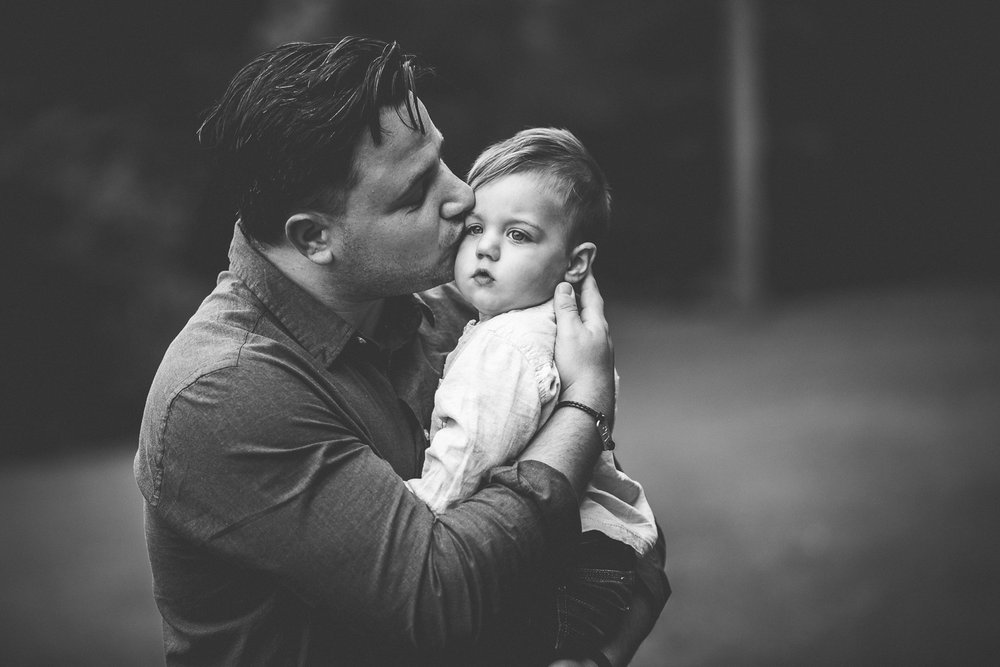 Father lovingly hugging and kissing his one year old son in outdoor family photoshoot in wimbledon