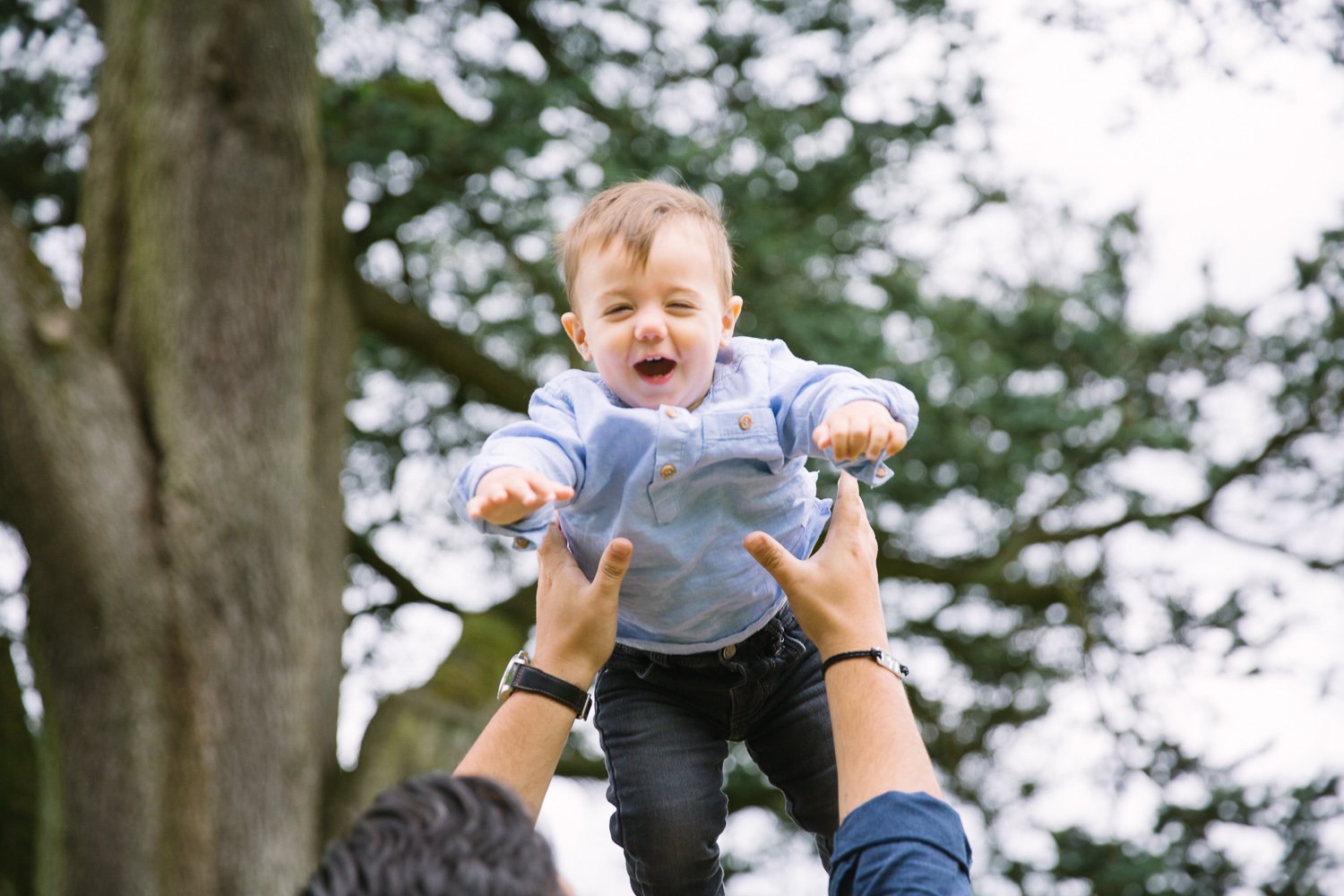 One year old laughing while flung in air by dad in outdoor family photoshoot in wimbledon