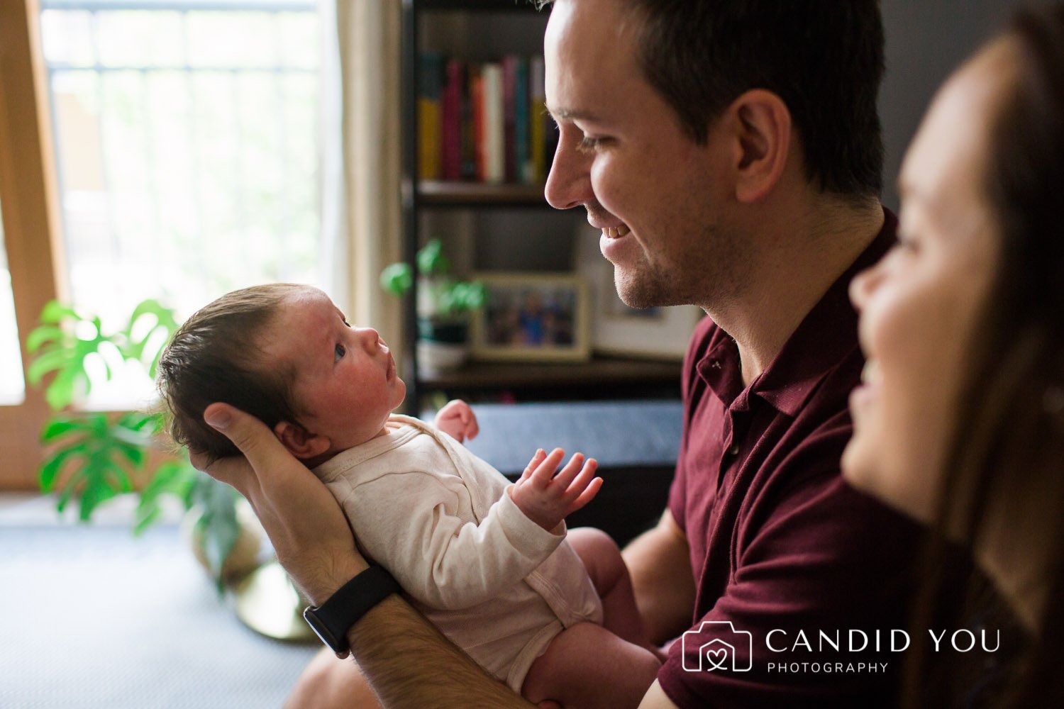 dad holding and smiling at newborn when mother looks on in twickenham