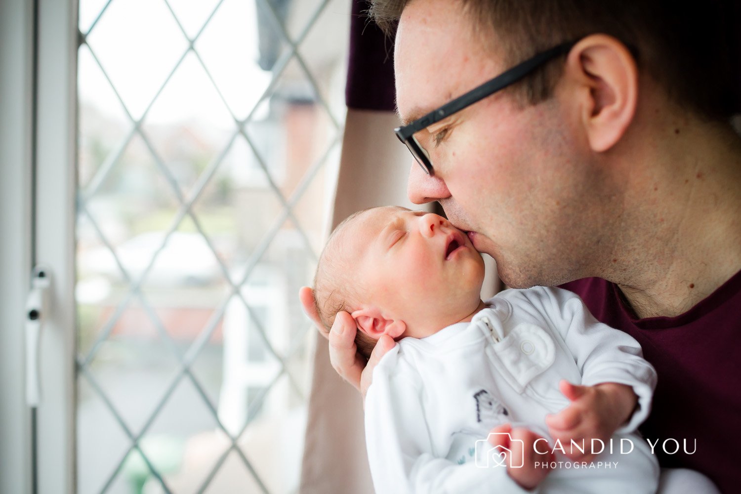 father kissing newborn with closed eyes