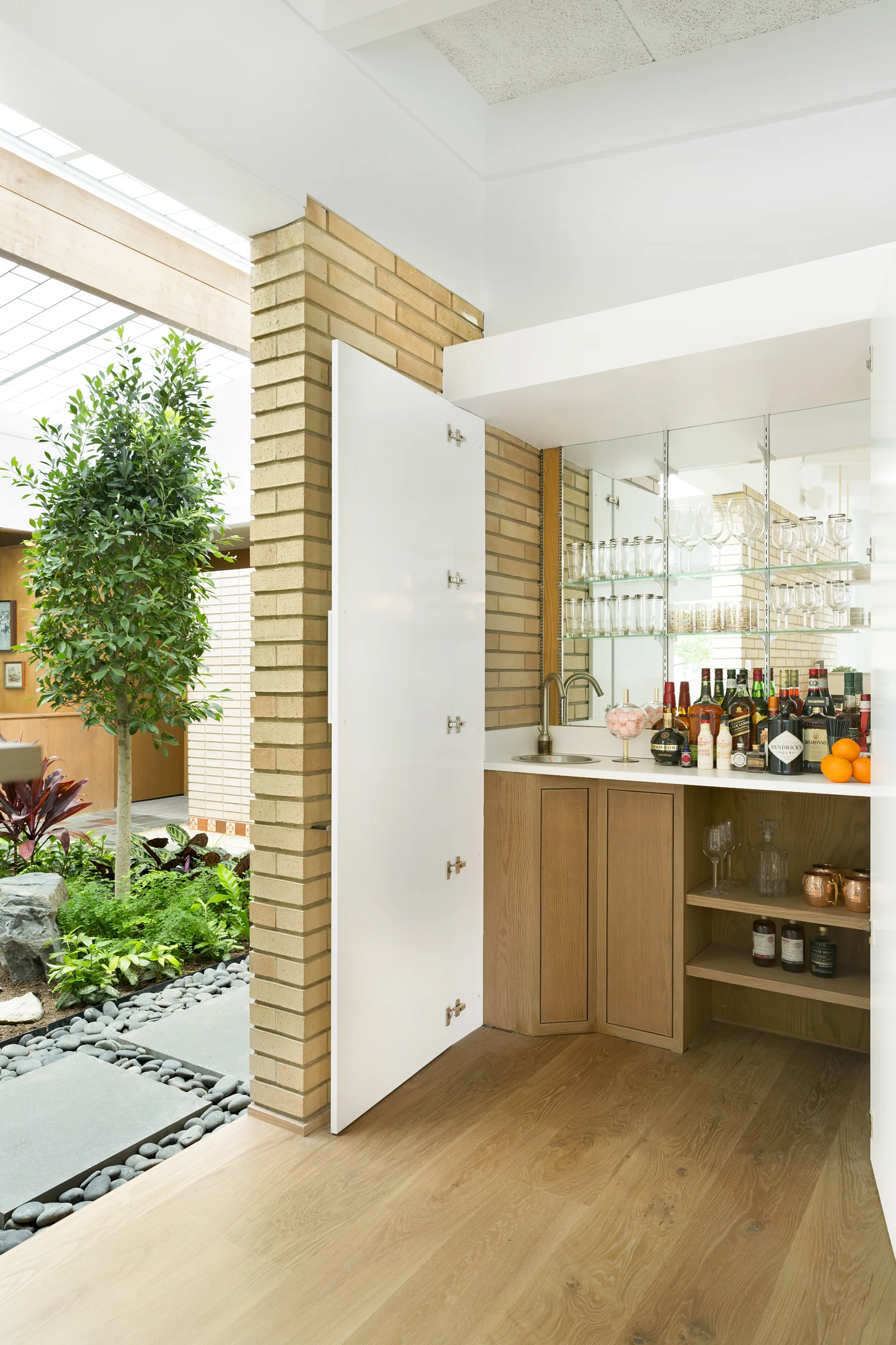 A hidden bar opens up onto an indoor atrium that has intentionally-placed obscured indoor views with a highly textured brick wall. In this space, there is even room for a koi pond, though it is not currently in use. Because this home has many windows and skylights, cloud movements affect the room lighting, changing throughout the day and creating varying light patterns in the process. / Design by Vela Creative , Photo by Spacecrafting