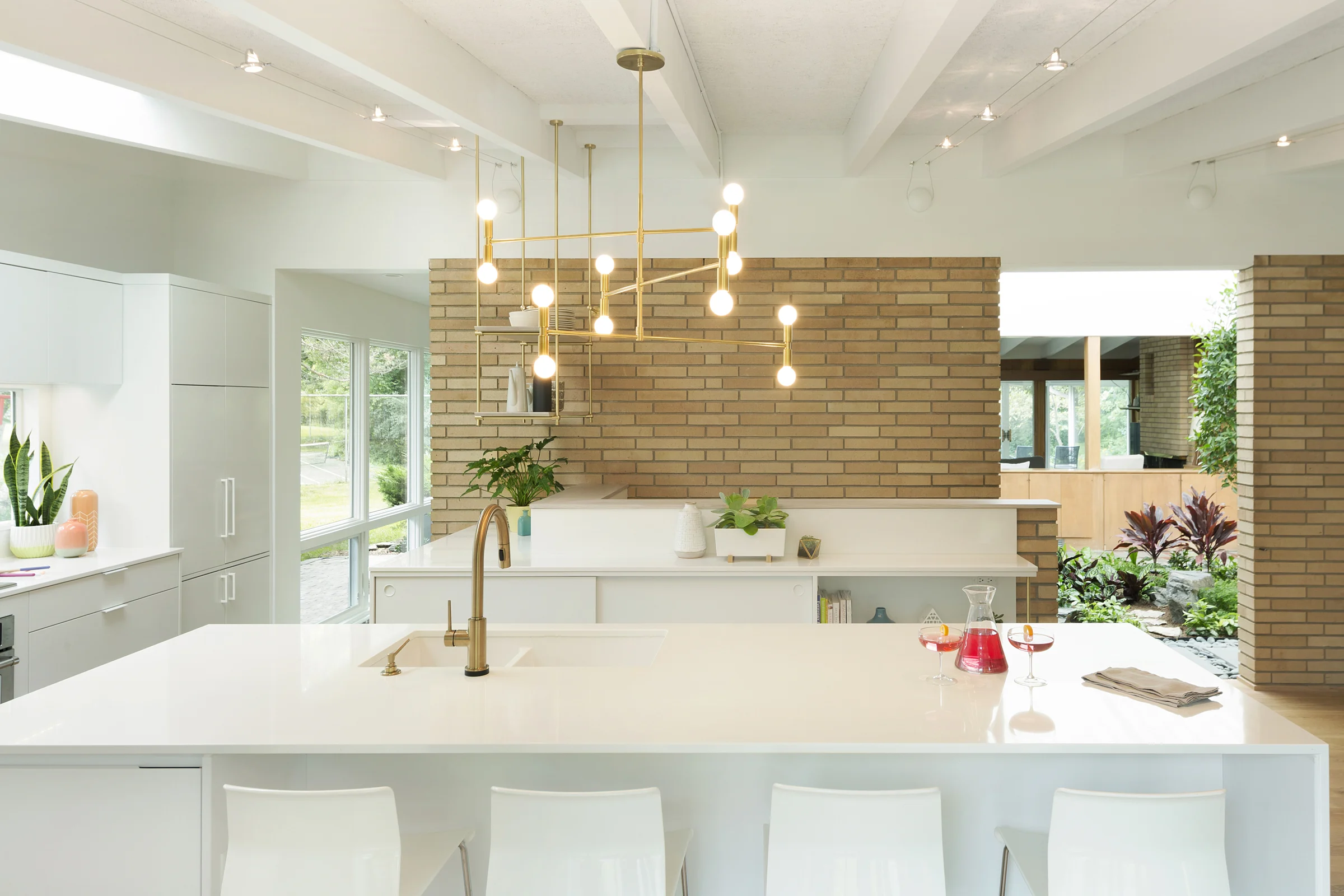 In our Arden Hills Midcentury Revitalization project, the home centers on an open-air indoor atrium (to the right of the kitchen island above). This space provides year-round foliage and abundant natural light, offering glimpses of changing weather patterns and shifting visually as the light changes throughout the day. / Source: Vela Creative