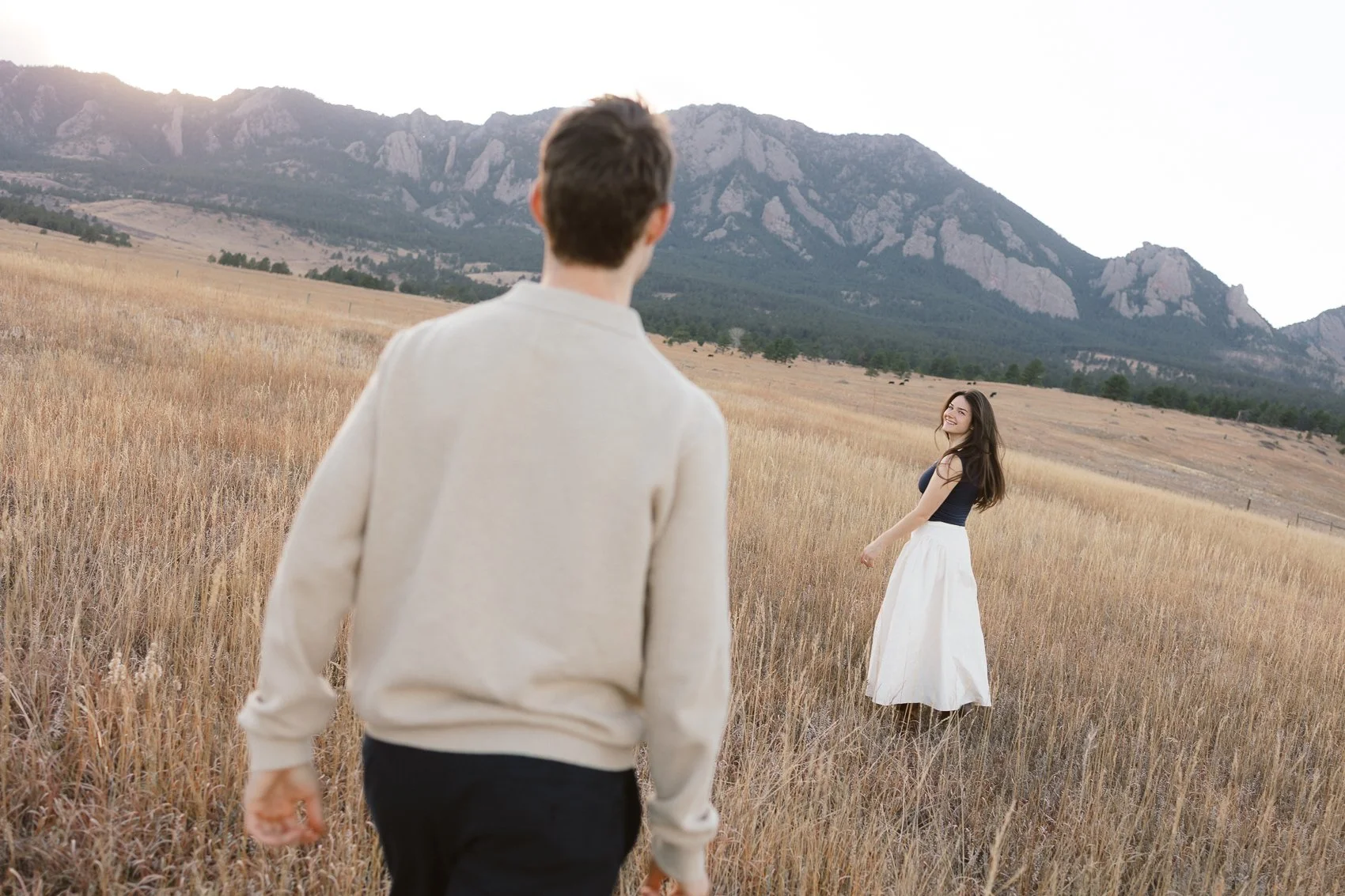 A woman looks back toward her fiance in a meadow in Boulder, Colorado engagement session.