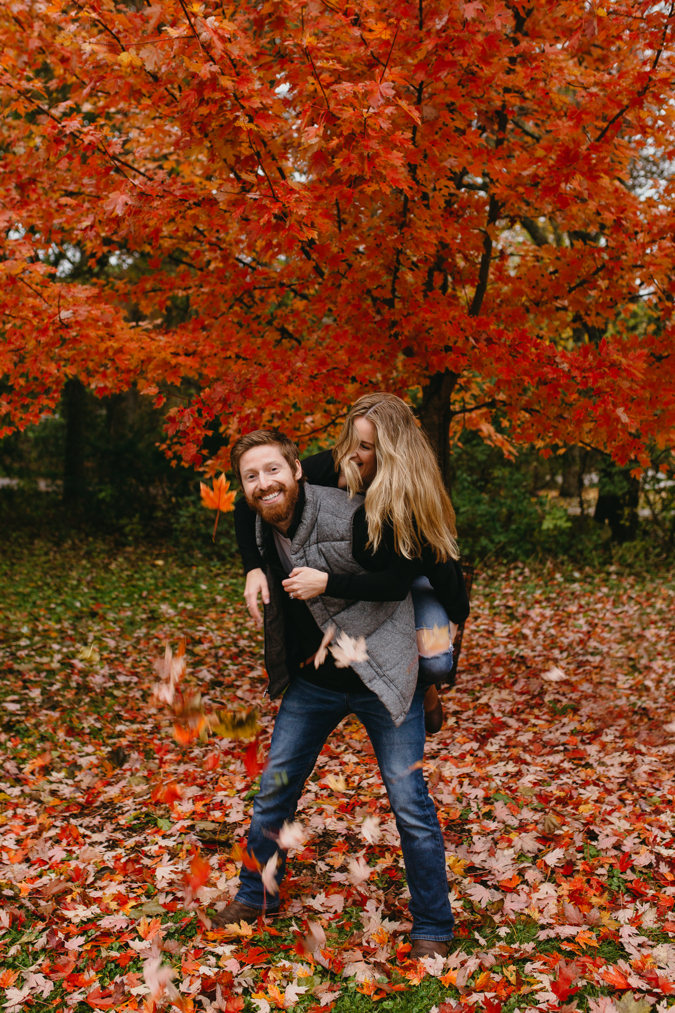 Engaged couple laughing and playing amidst bright red leaves in fall in Chicago.