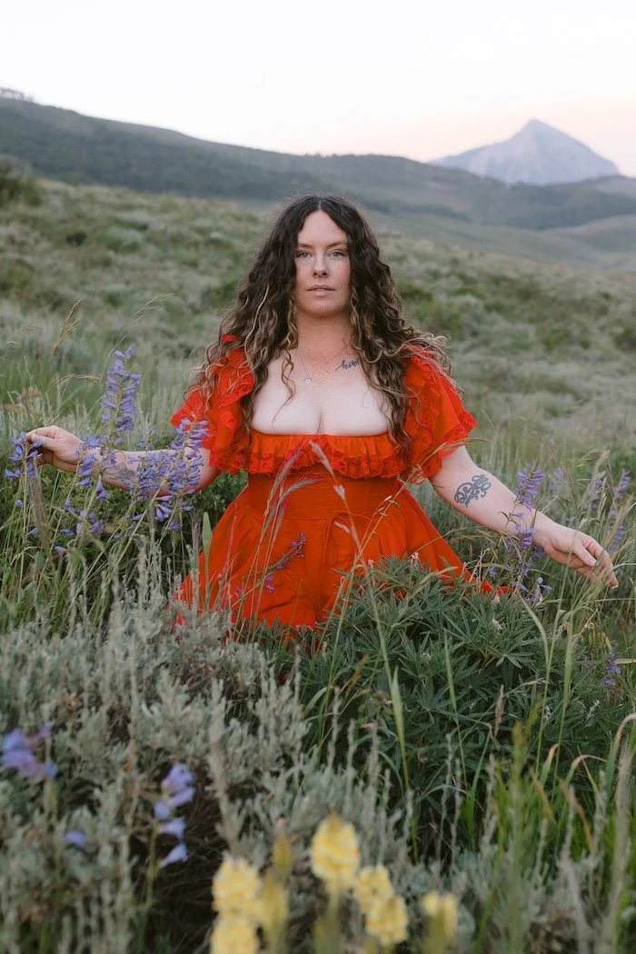 A woman in a red dress sits among a field of wildflowers in Crested Butte, Colorado wedding photographer.
