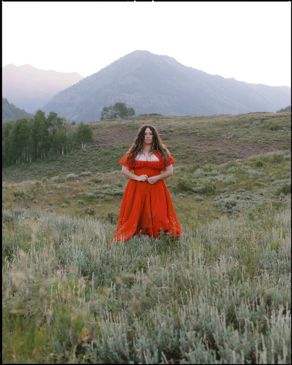 A woman stands in the Crested Butte mountains wearing a red, Selkie dress, Colorado wedding photographer.