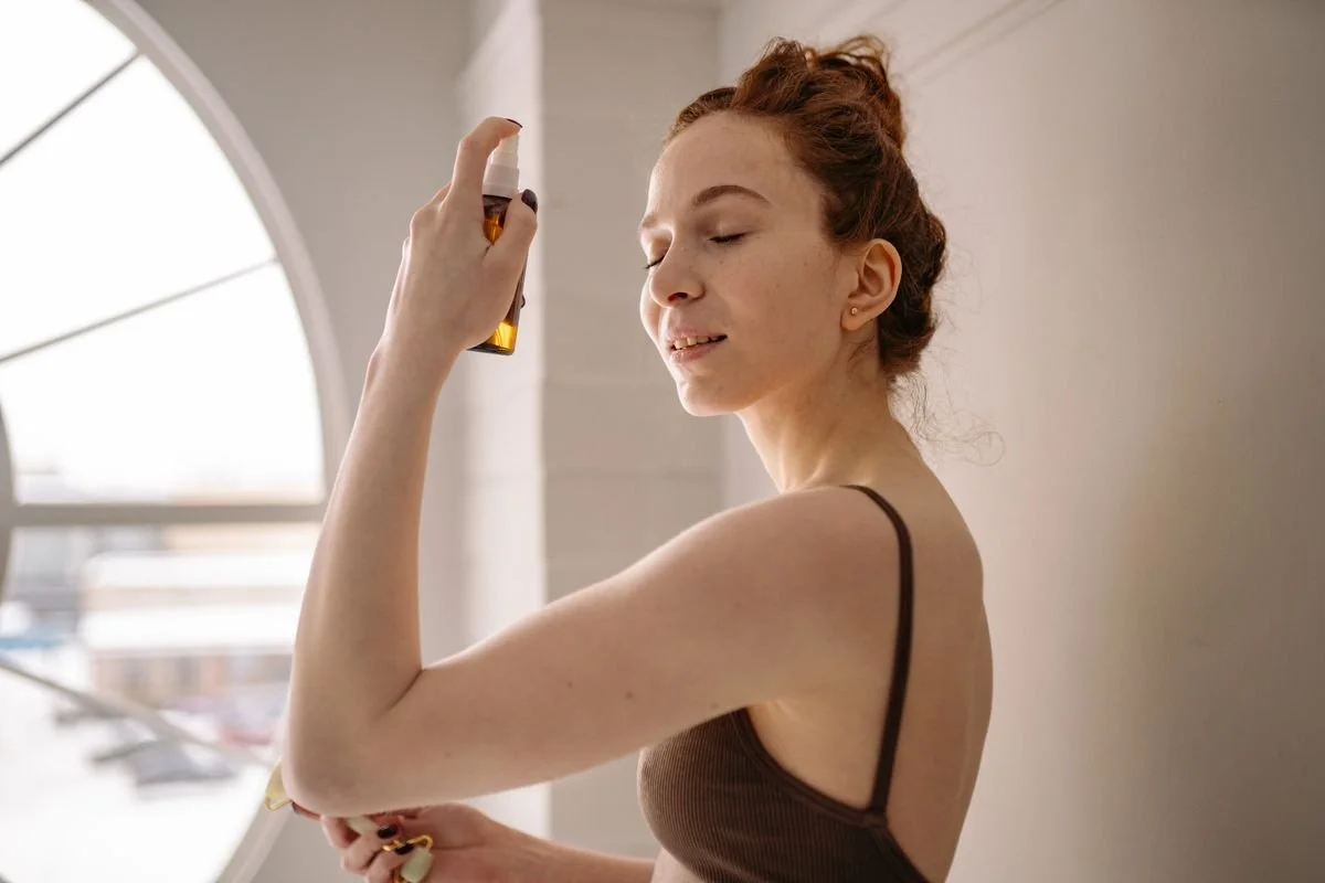 Woman misting her face with a hydrating spray in front of a bright indoor window