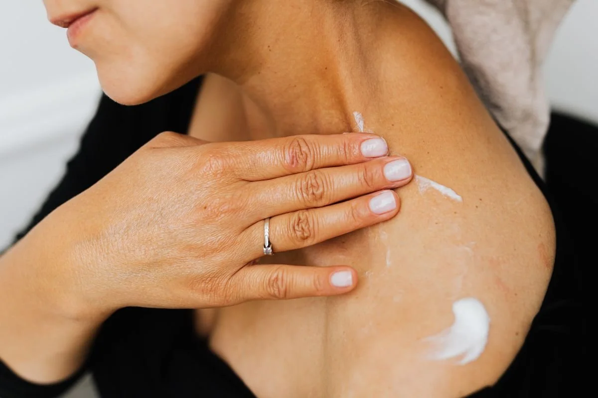 Close view of a woman smoothing moisturizing cream across her shoulder and collarbone