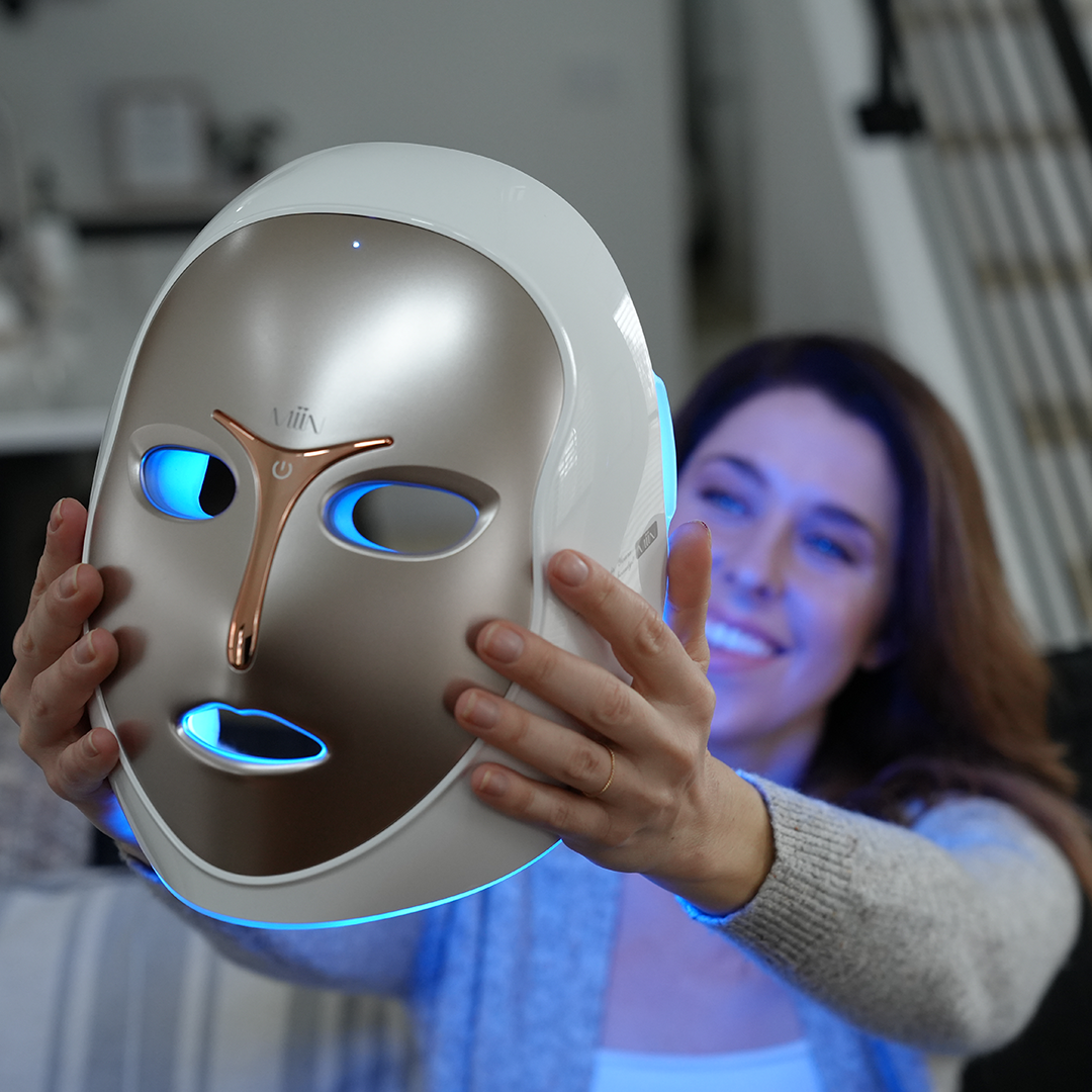 LED face mask lit blue being held up at home, showing the eye and nose detailing