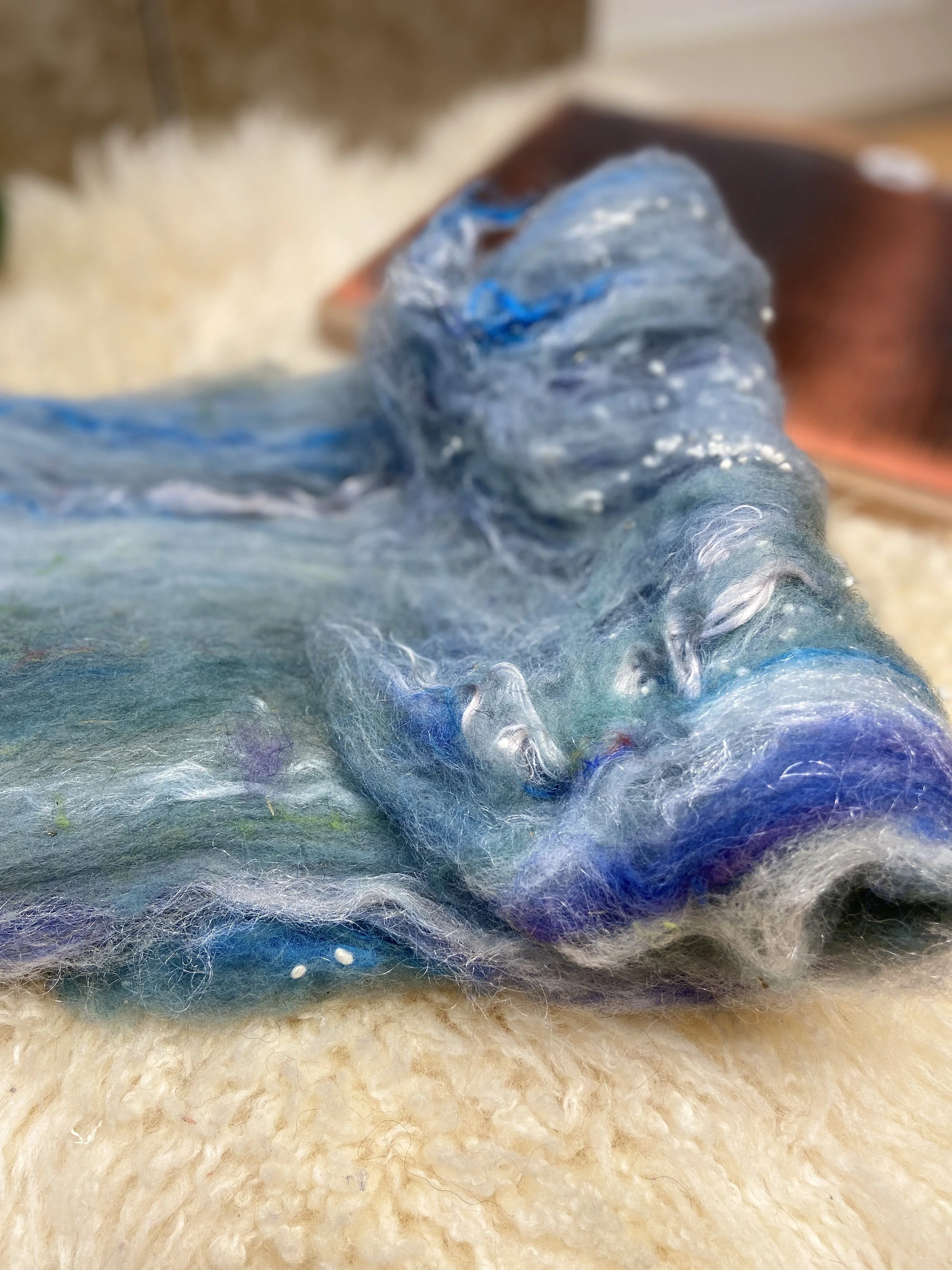 a hand. blended batt of multiple fibers used for felting and spinning yarn