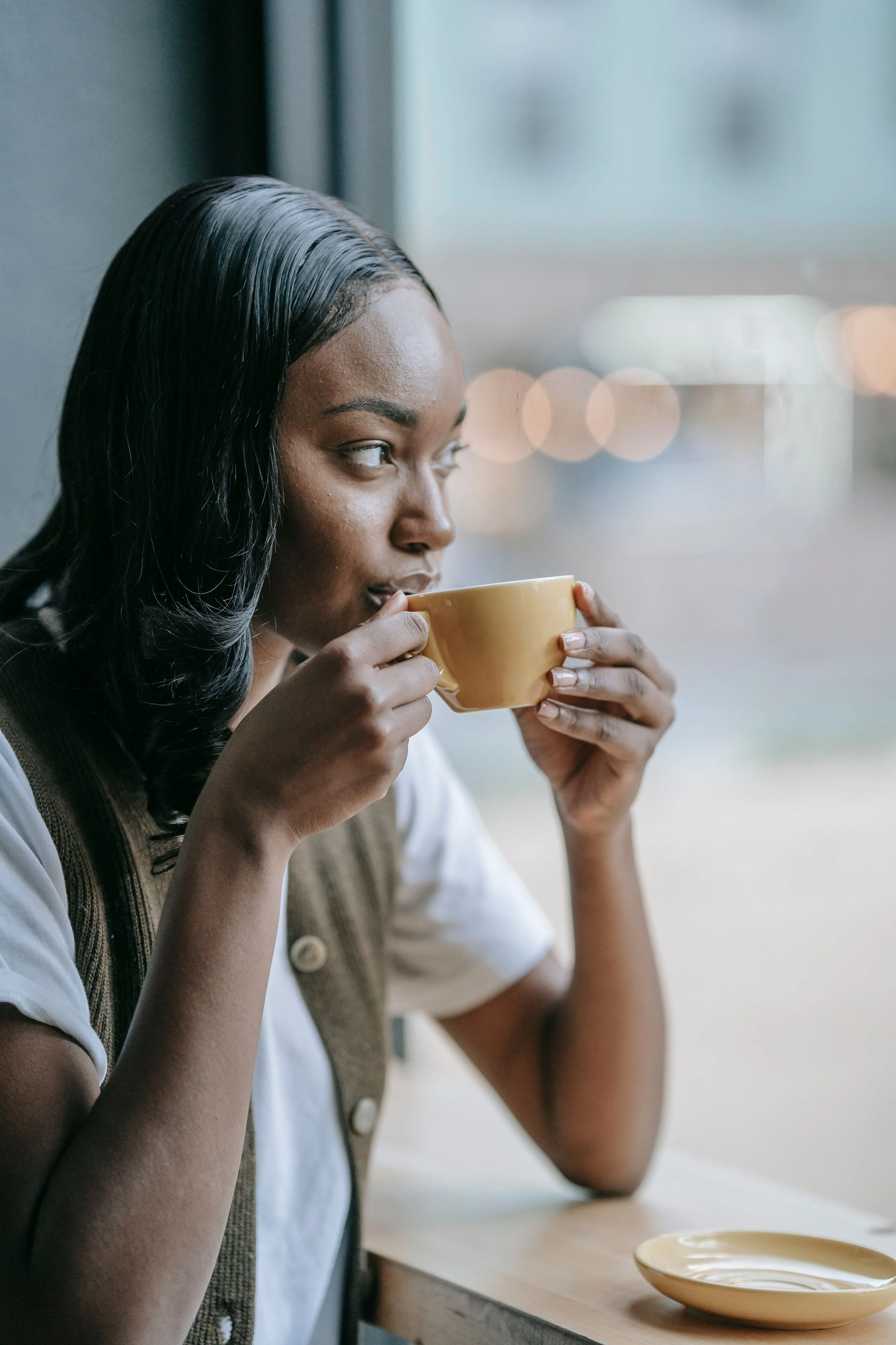 Black woman sitting in coffee shop, drinking coffee and looking our window