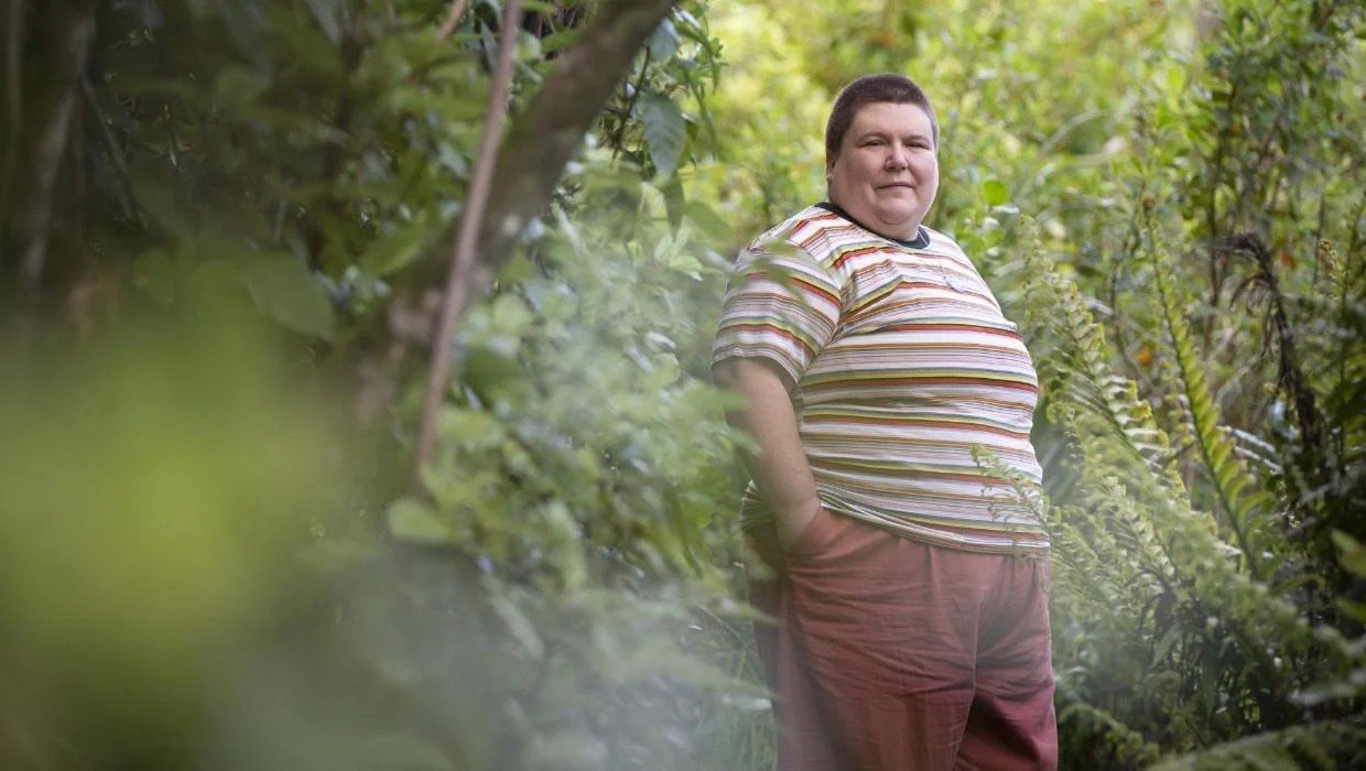 colour photo of Andi Buchanan wearing a striped t-hirt and trousers surrounded by native bush
