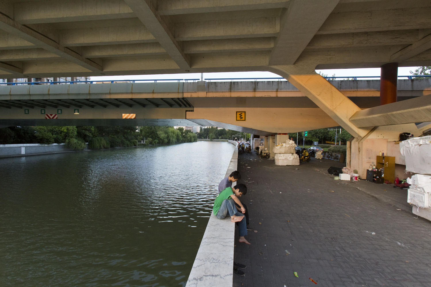 Two teens sitting underneath a bridge which crosses Suzhou Creek. Shanghai, China. 2016.