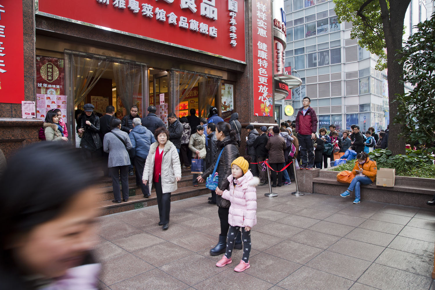 A young girl in a yellow hat standing in the midst of a crowded Nanjing East Road. Shanghai, China. 2014. 