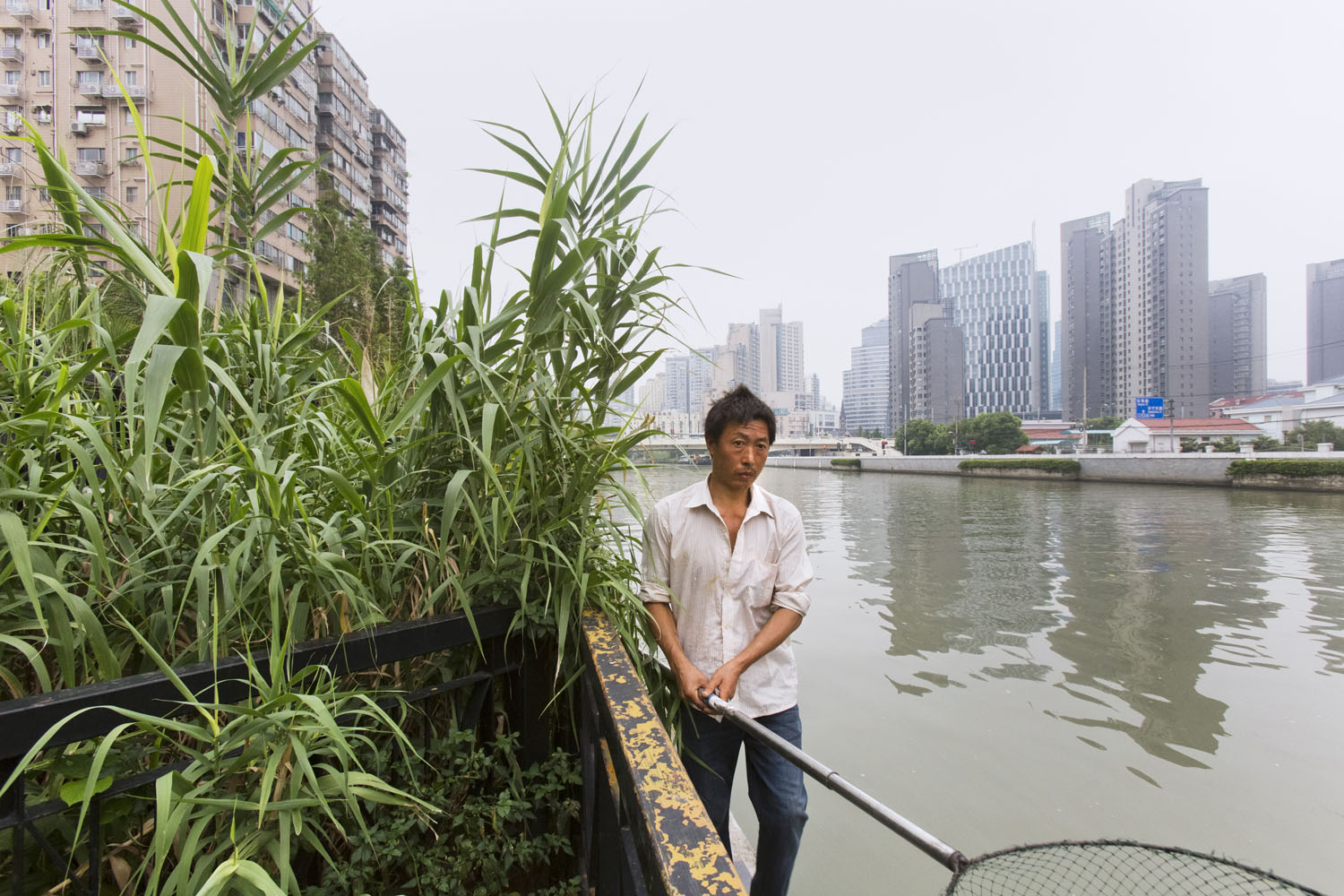 Net fisherman walking the edge of Suzhou Creek. Shanghai, China. 2016.