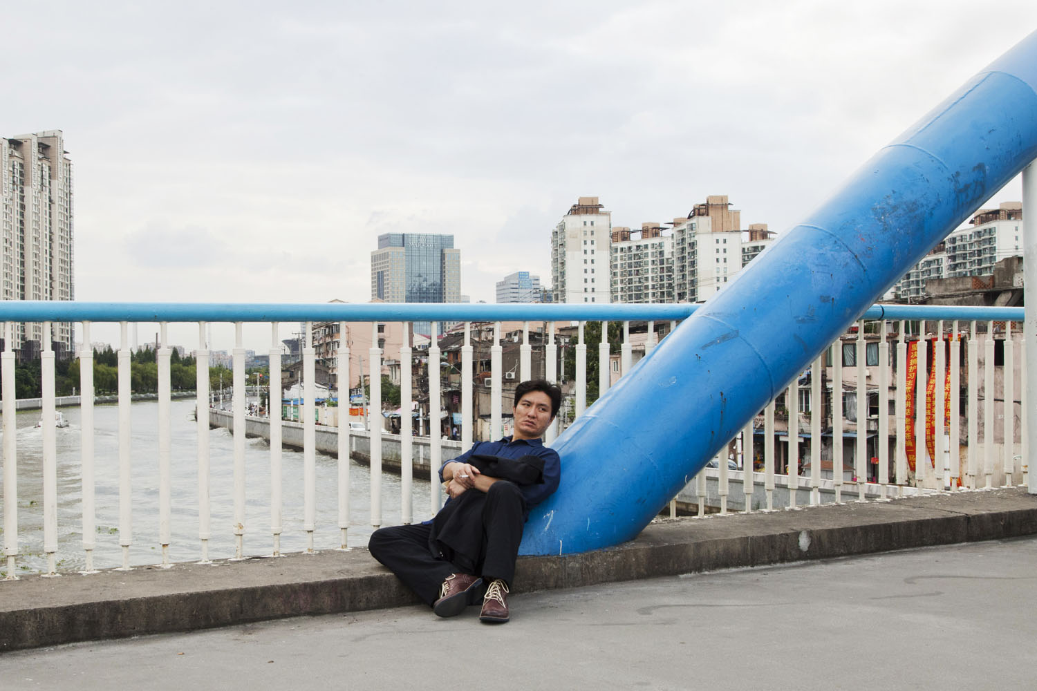 Man sitting on a bridge which crosses Suzhou Creek. Shanghai, China. 2015.