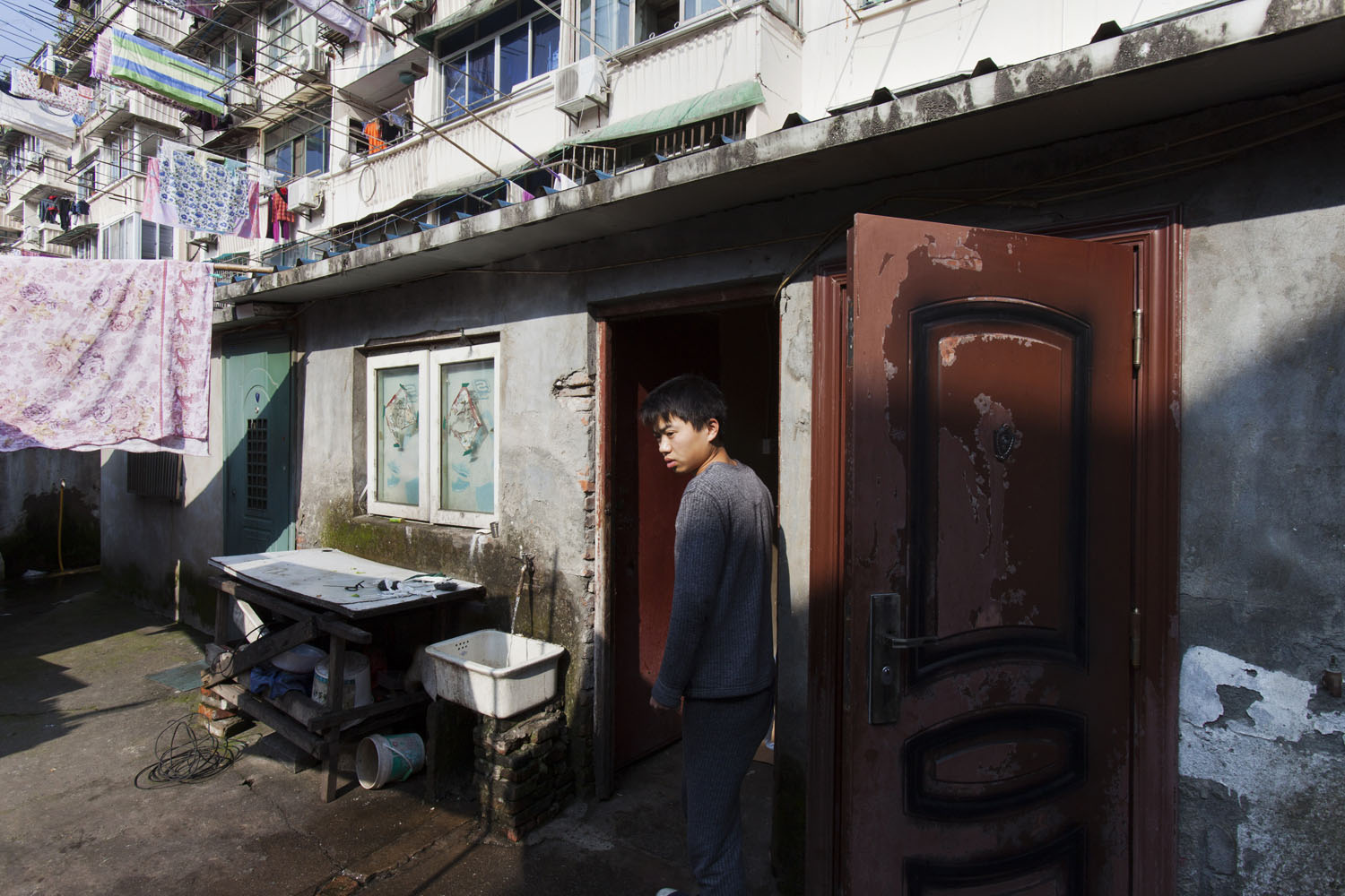 Young man walks by the front door that leads to his rented apartment.  Guangfu Road. Shanghai, China. 2015.