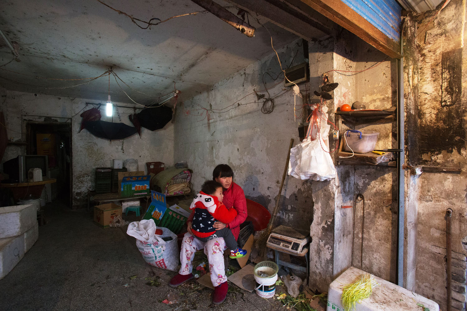 Woman sits inside her family's makeshift storefront with her son. Guangfu Road. Shanghai, China. 2015.