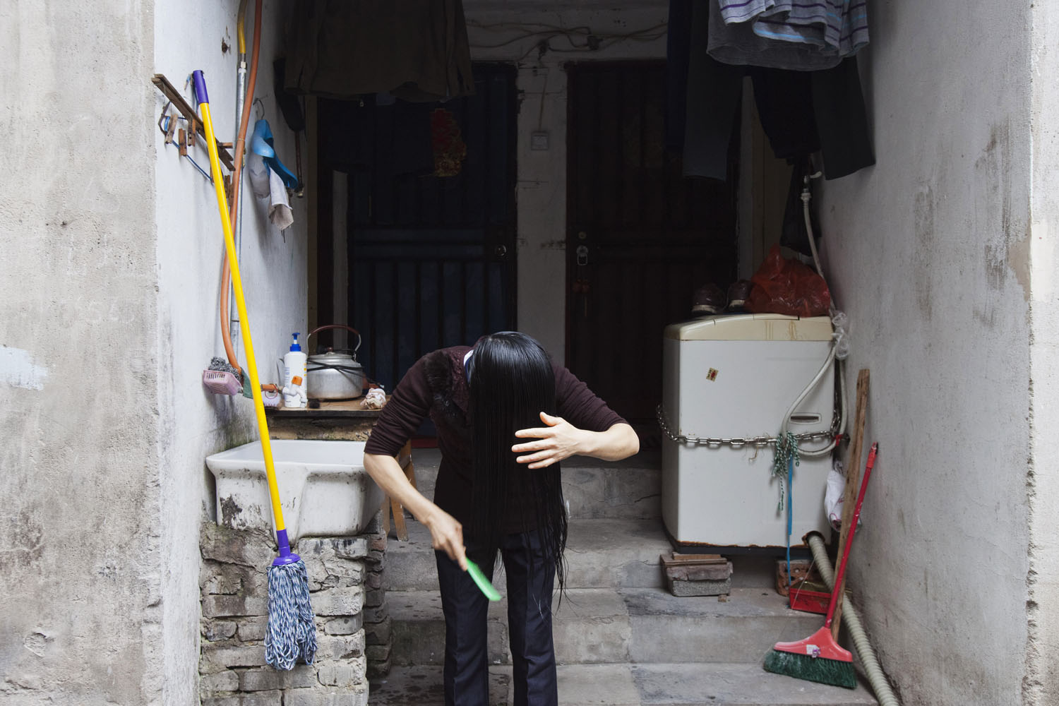 A woman washes and brushes her hair in front of her home. Guangfu Road. Shanghai, China. 2015.