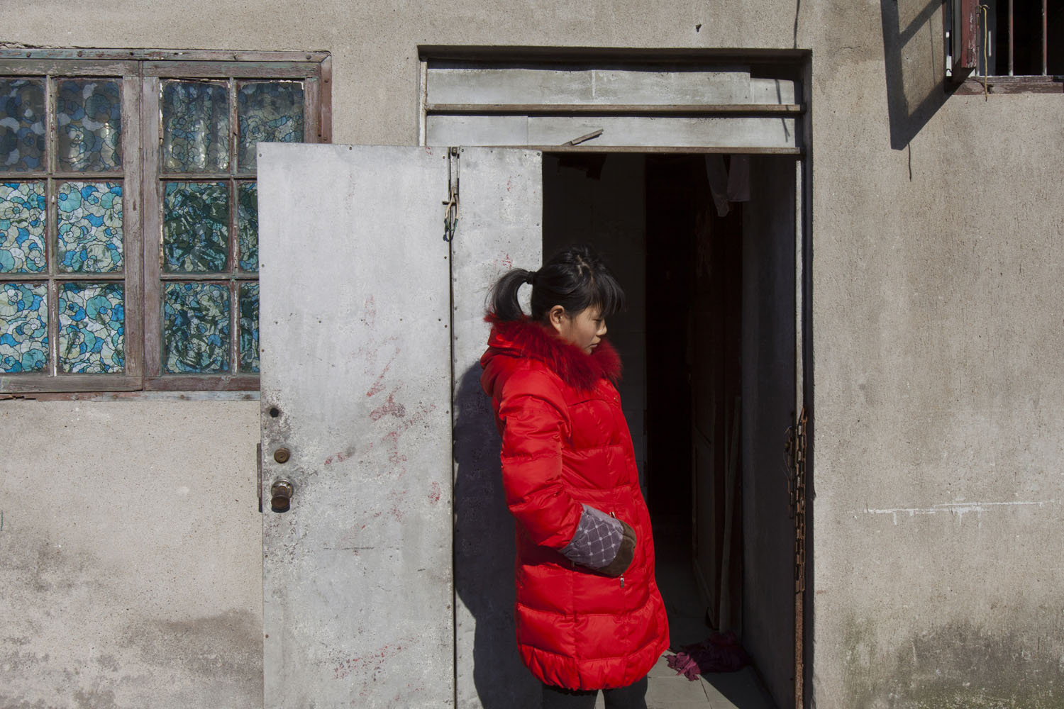 Young woman in a red jacket stands in front of an old lane house. Guangfu Road. Shanghai, China. 2015.
