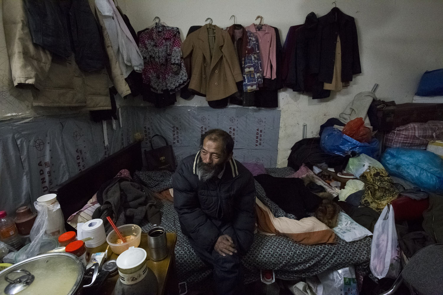 A man sits for a portrait after dinner in the rented rooms that he shares with his wife. Guangfu Road. Shanghai, China. 2016.