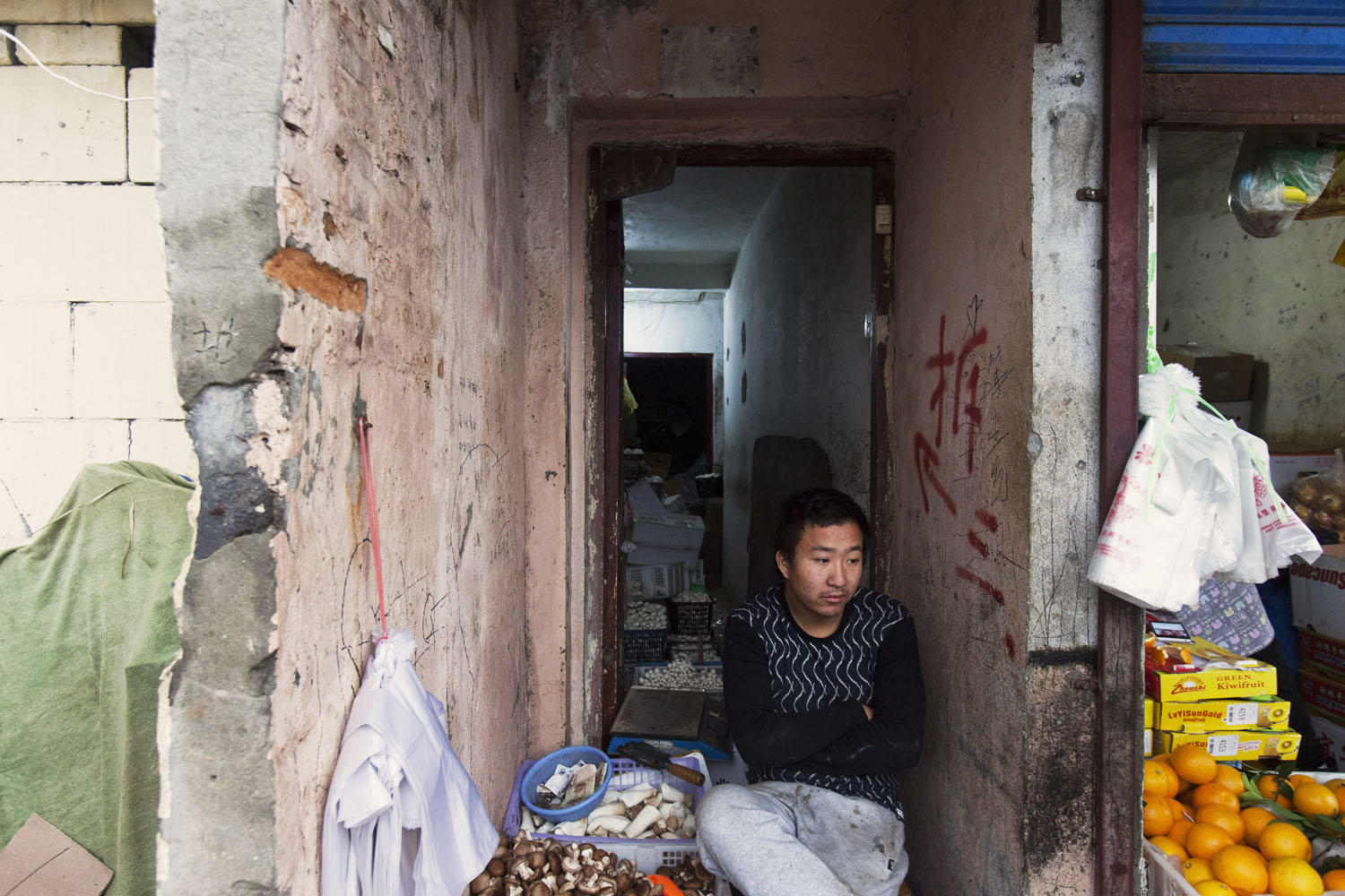 Merchant sits outside of his makeshift fruits and vegetables shop, that is soon to be removed from the main road. Guangfu Road. Shanghai, China. 2015.