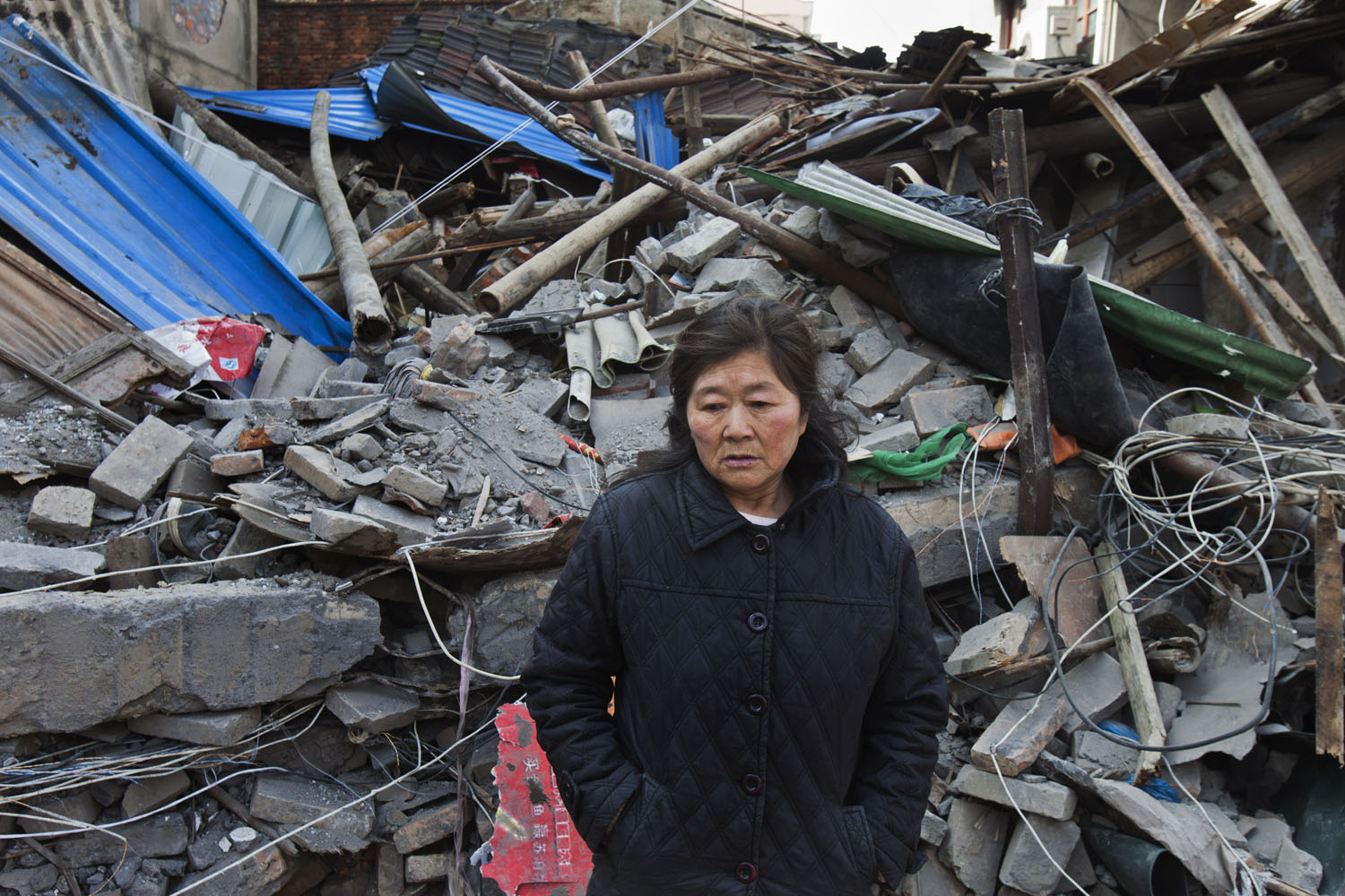 Woman stands for a portrait in front of the demolished rented apartment where she stayed for many years, after a forcible eviction and demolition. Guangfu Road. Shanghai, China. 2015.