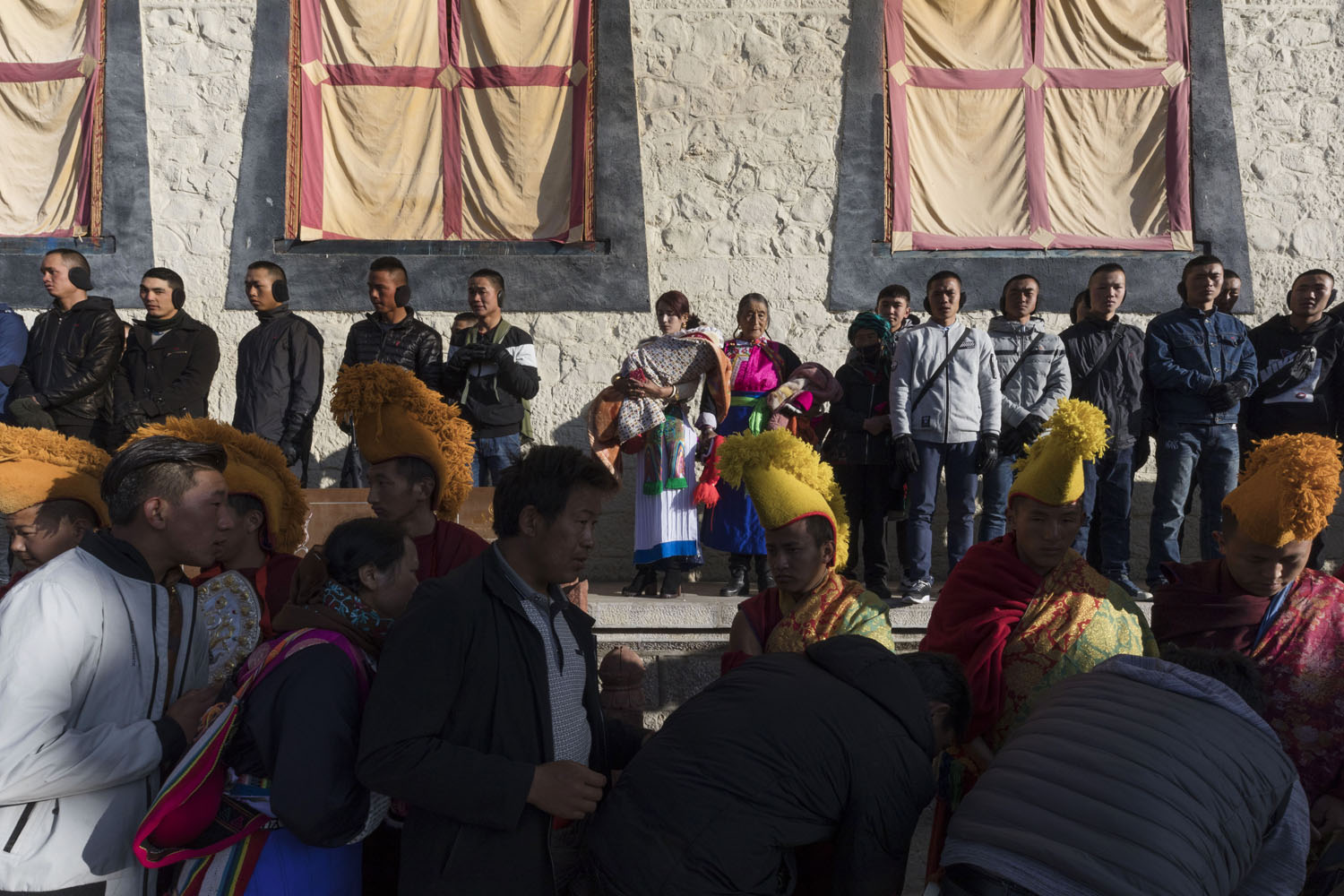 Woman in traditional clothing watches, while plain clothed authorities stand on either side of her in observation at SongZangLin Monastery in JingXiang Village. Yunnan, China. March 2, 2018.