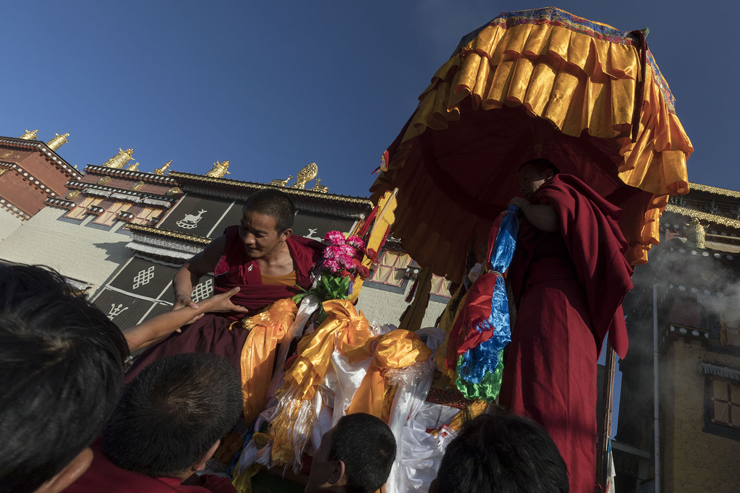 Tibetan Buddhist monks emerge from the monastery with a chatra that is carrying two monks, at SongZangLin Monastery in JingXiang Village. Yunnan, China. March 2, 2018.