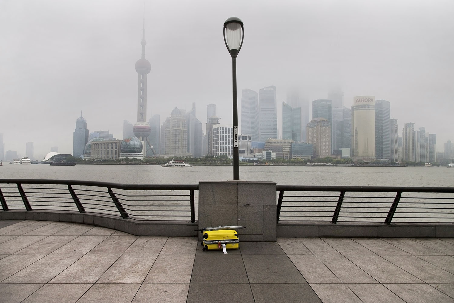 Yellow suitcase and an umbrella on The Bund, with Lujiazui in the background. Shanghai, China. 2013.