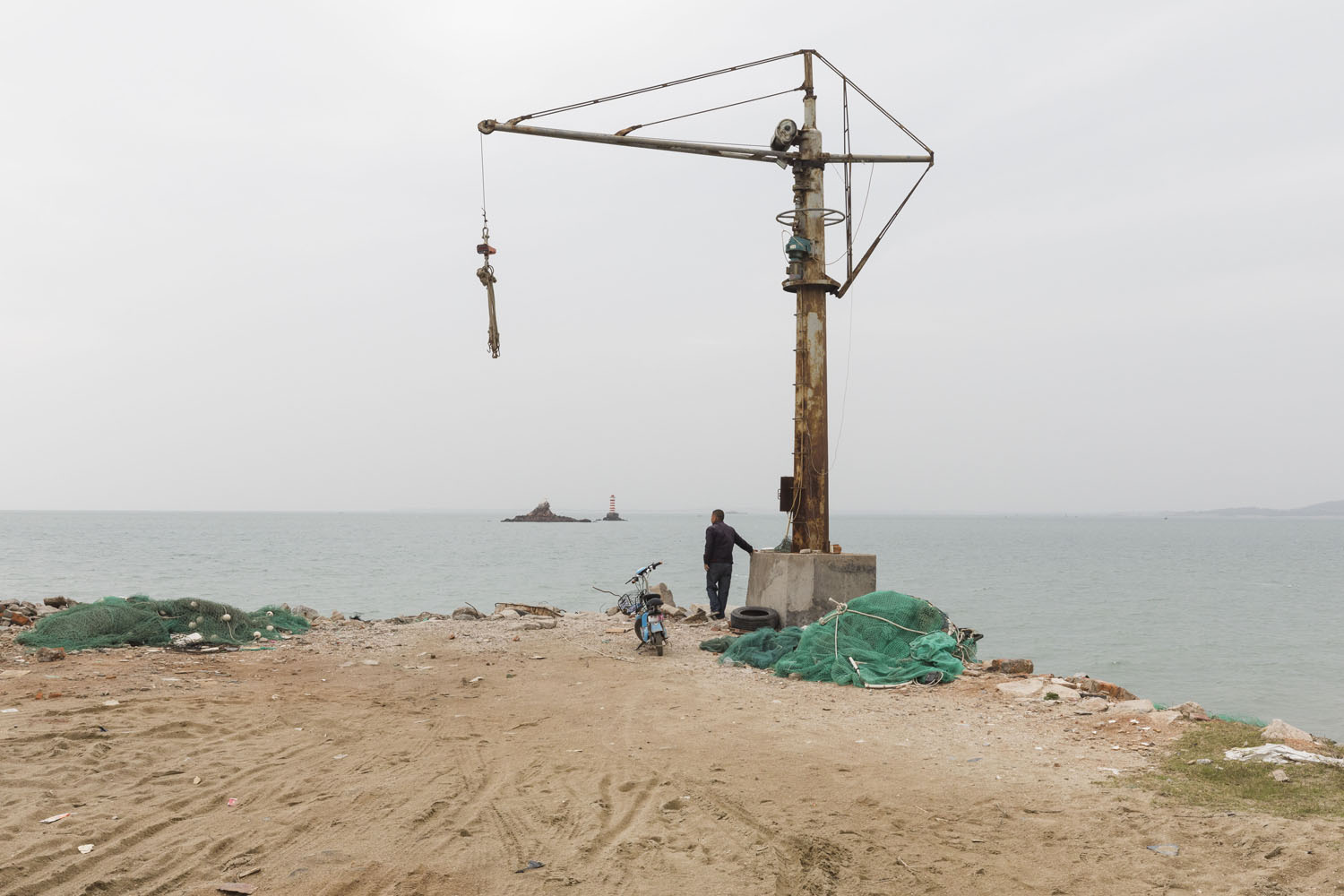 Man stands next to an old crane overlooking Guanyinshan Fantasy Beach. Xiamen, China. 2018.