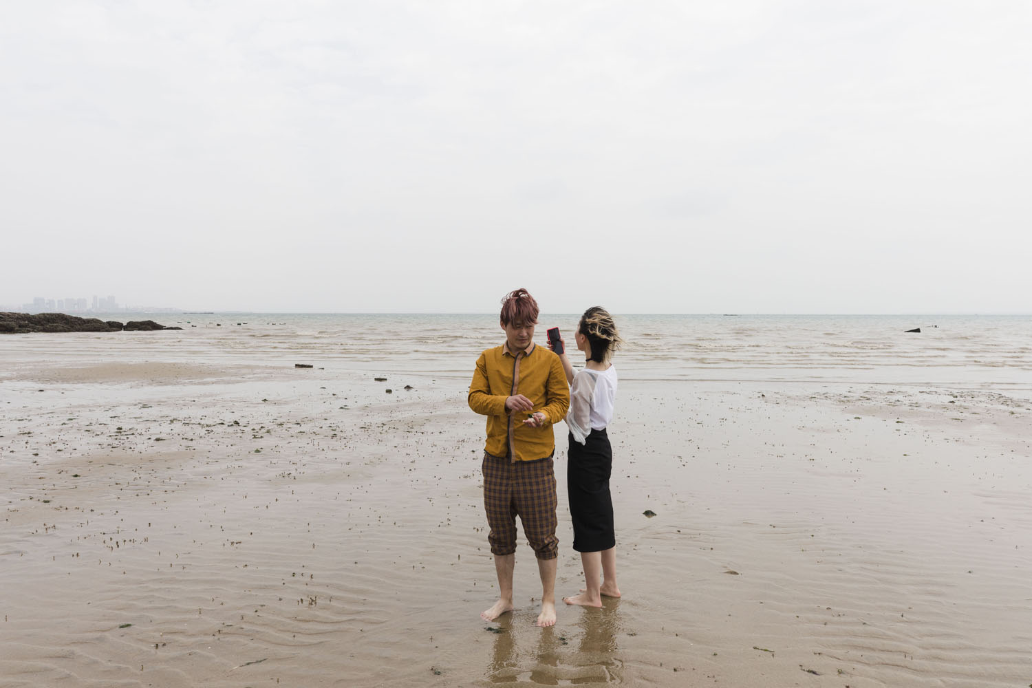 A couple stand for a photograph while looking for seashells at Guanyinshan Fantasy Beach. Xiamen, China. 2018.