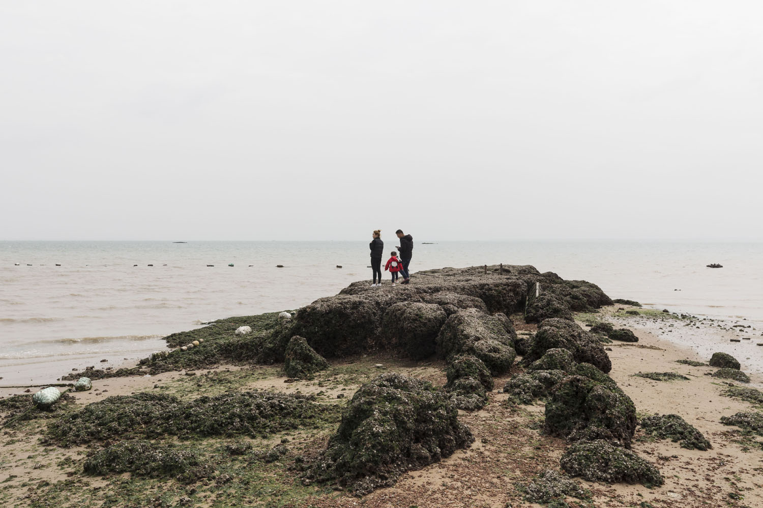 A family walk and climb among the rocky shore at Guanyinshan Fantasy Beach. Xiamen, China. 2018.