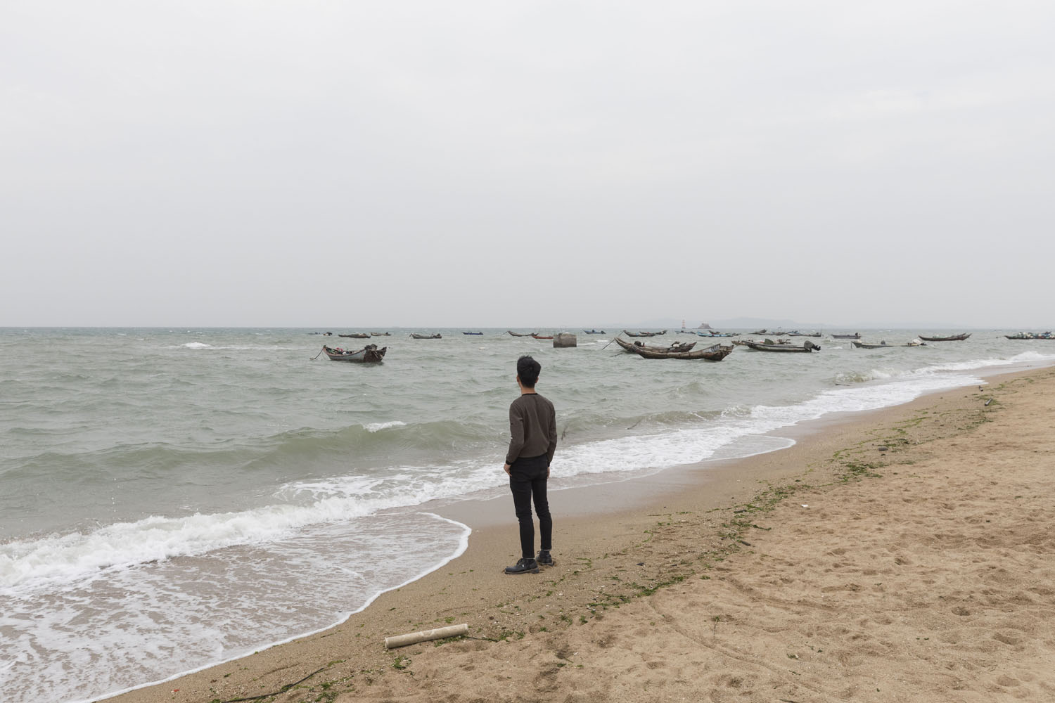 Man looks out toward the ocean at Guanyinshan Fantasy Beach. Xiamen, China. 2018.